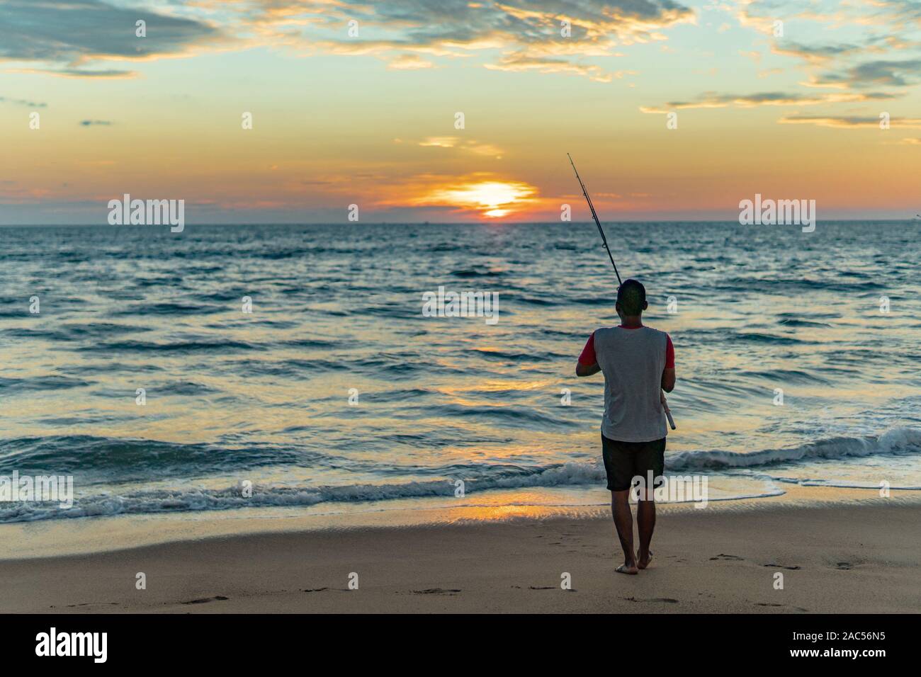 Mann mit Angelrute steht auf sandigen Strand bei Sonnenuntergang in Goa, Indien Stockfoto