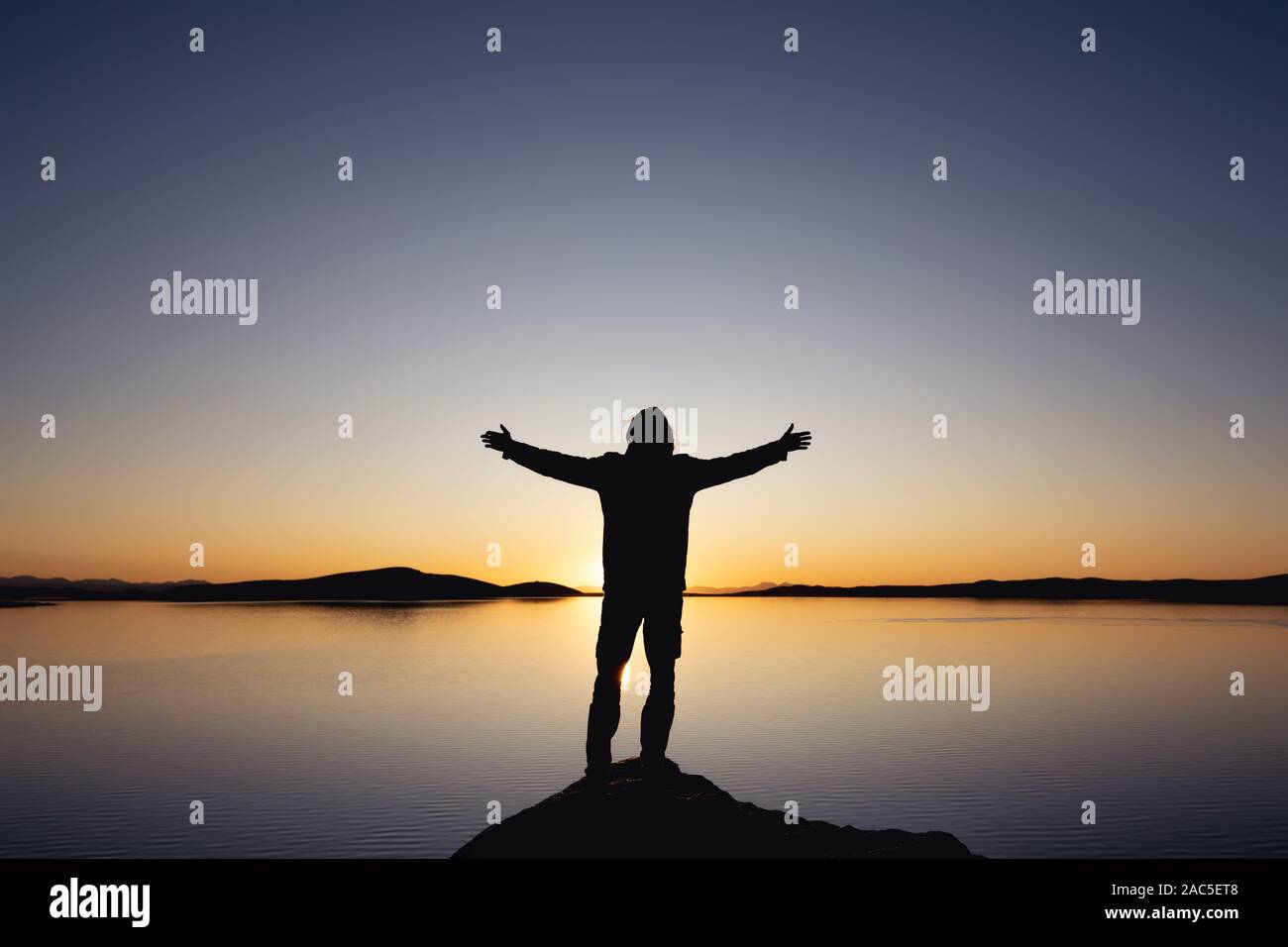 Der Mensch Silhouette steht mit erhobenen Armen gegen Sonnenuntergang See und Berge Stockfoto