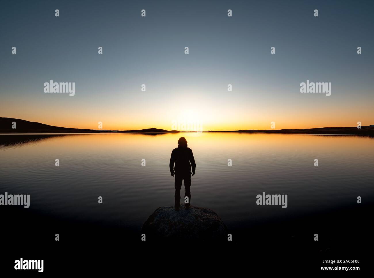 Einsame Silhouette des Menschen steht auf Big Rock bei Sonnenuntergang See und blickt auf die Berge Stockfoto