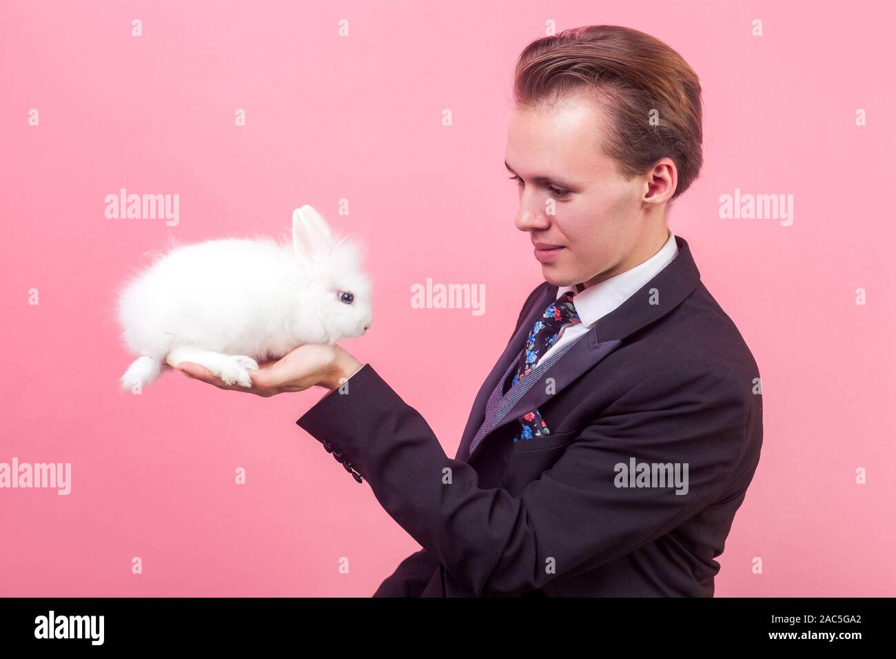 Pet Adoption. Porträt der jungen positiver Mann im eleganten Anzug und mit stilvollen Frisur an adorable White Rabbit auf seiner Hand suchen, Haustier. Stockfoto