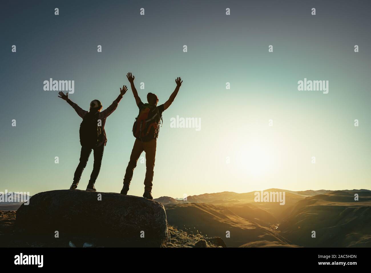 Zwei glückliche Wanderer steht mit erhobenen Armen gegen Sonnenuntergang und genießt Berge Stockfoto