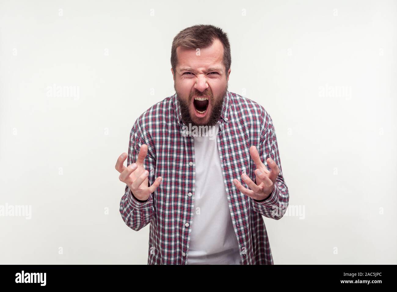 Portrait von aggressiven bärtiger junger Mann in Plaid Shirt stehend mit wütenden Gesicht voller Hass und Zorn, starke Emotionen erleben, schreien. Ich Stockfoto