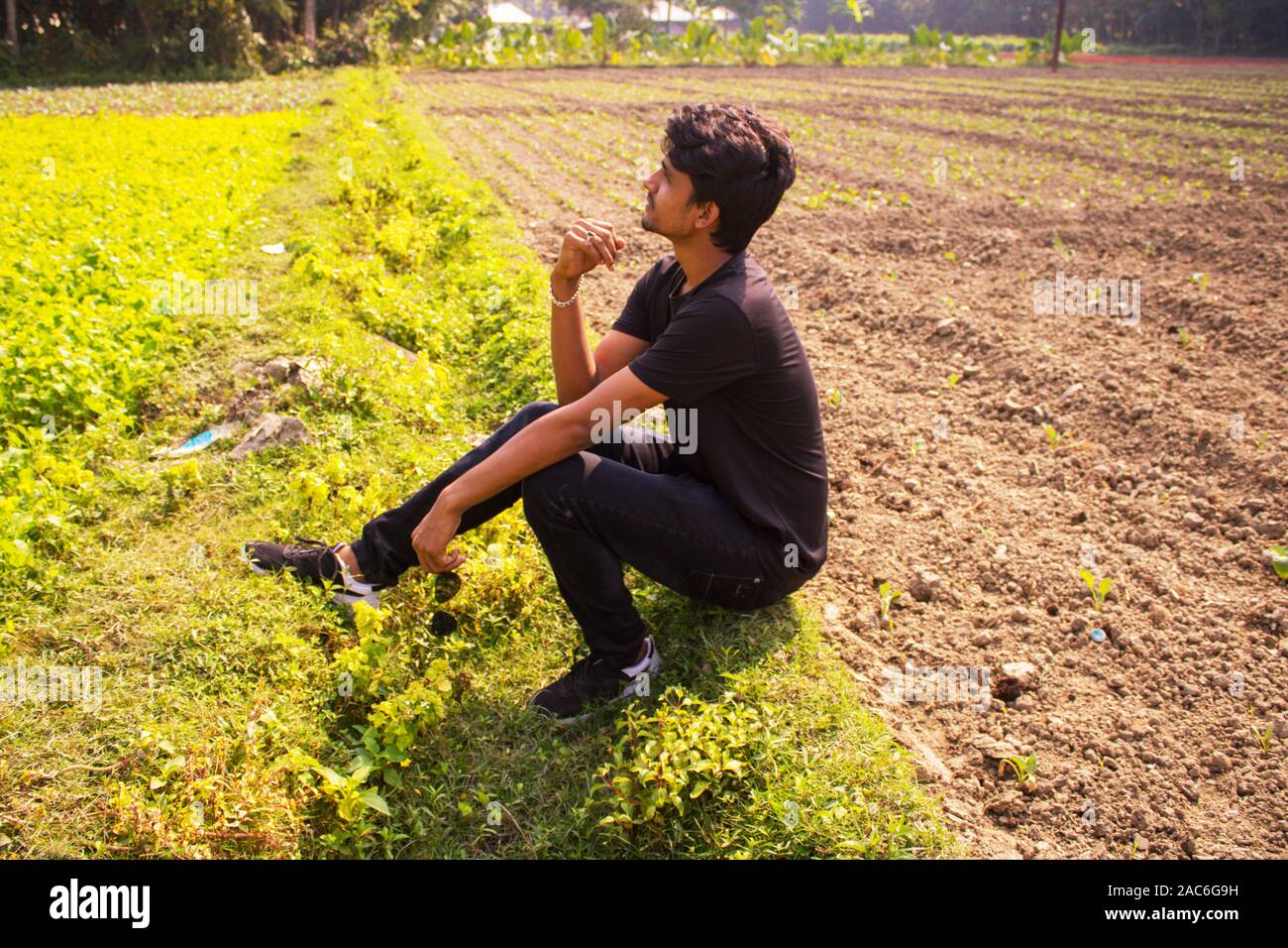 Ein kleiner Junge sitzt auf Feld ist und denken Tief oder Spannung, Hintergrund ist die Natur Stockfoto