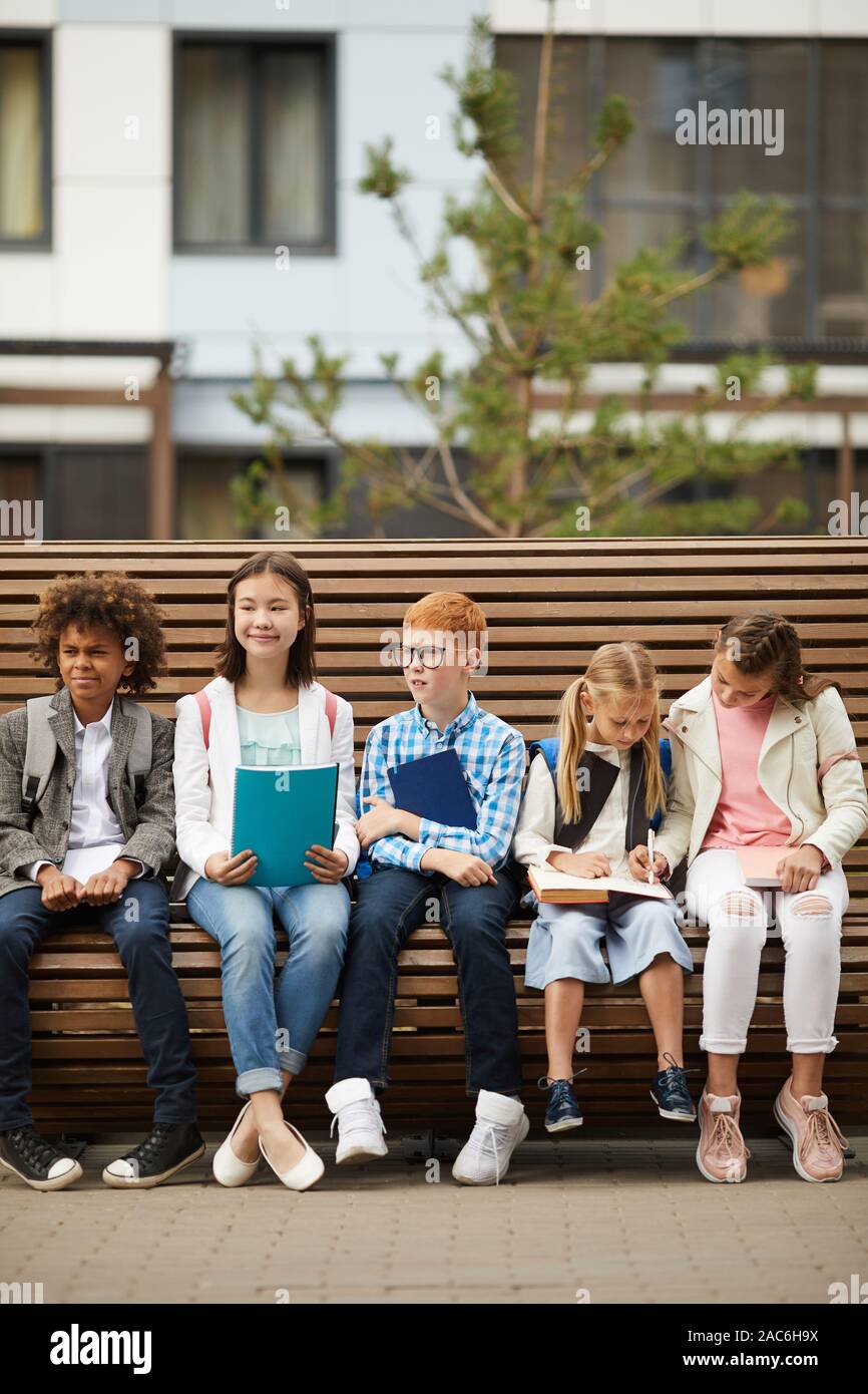 Gruppe von multiethnischen Schule Kinder auf der Bank sitzen mit Lehrbüchern und Notebooks und die Vorbereitung für den Unterricht im Freien Stockfoto