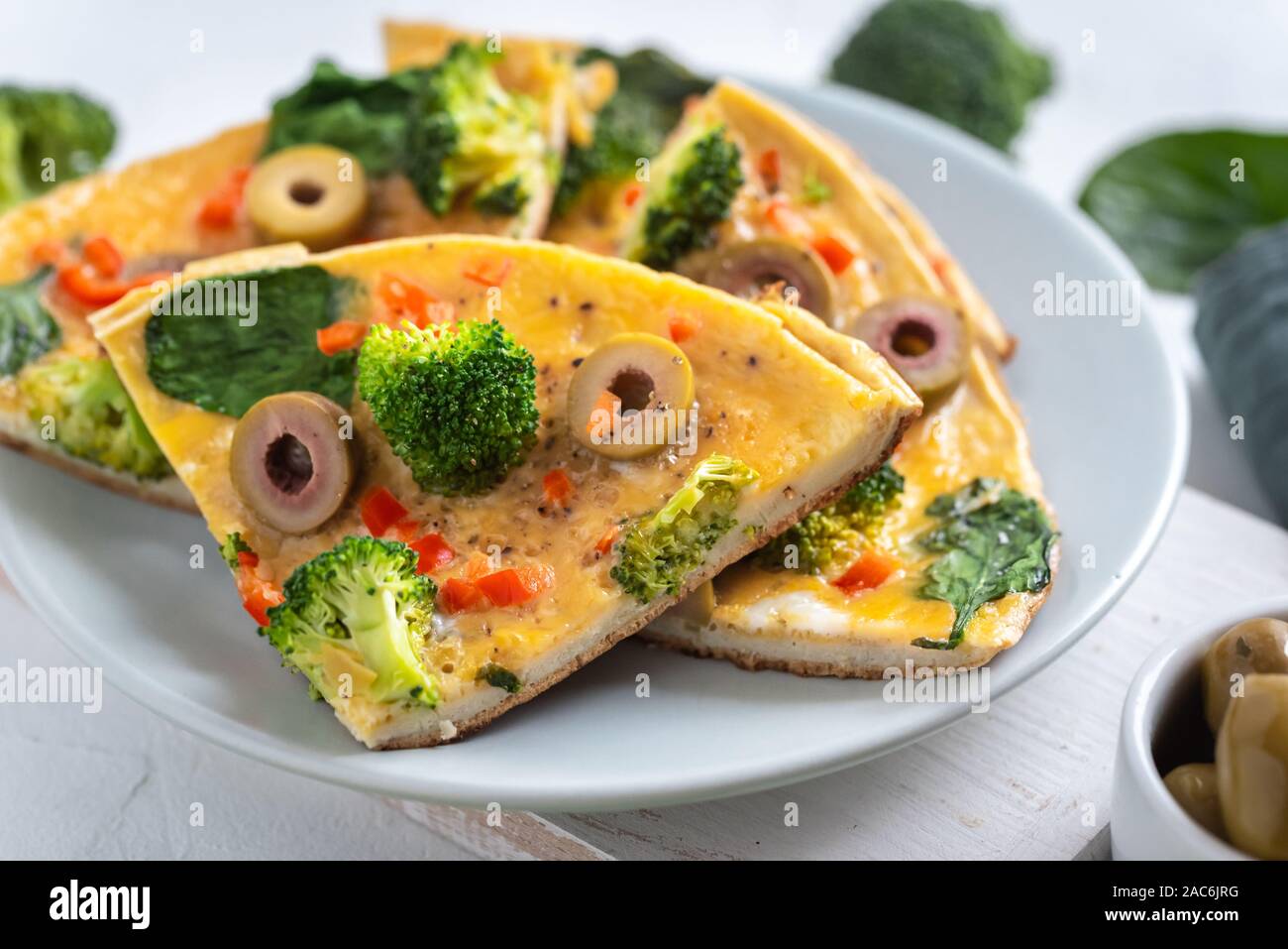 Omelette mit Brokkoli, Spinat und Oliven auf einem Teller. Frittata - italienisches Omelett mit grünem Gemüse. Stockfoto