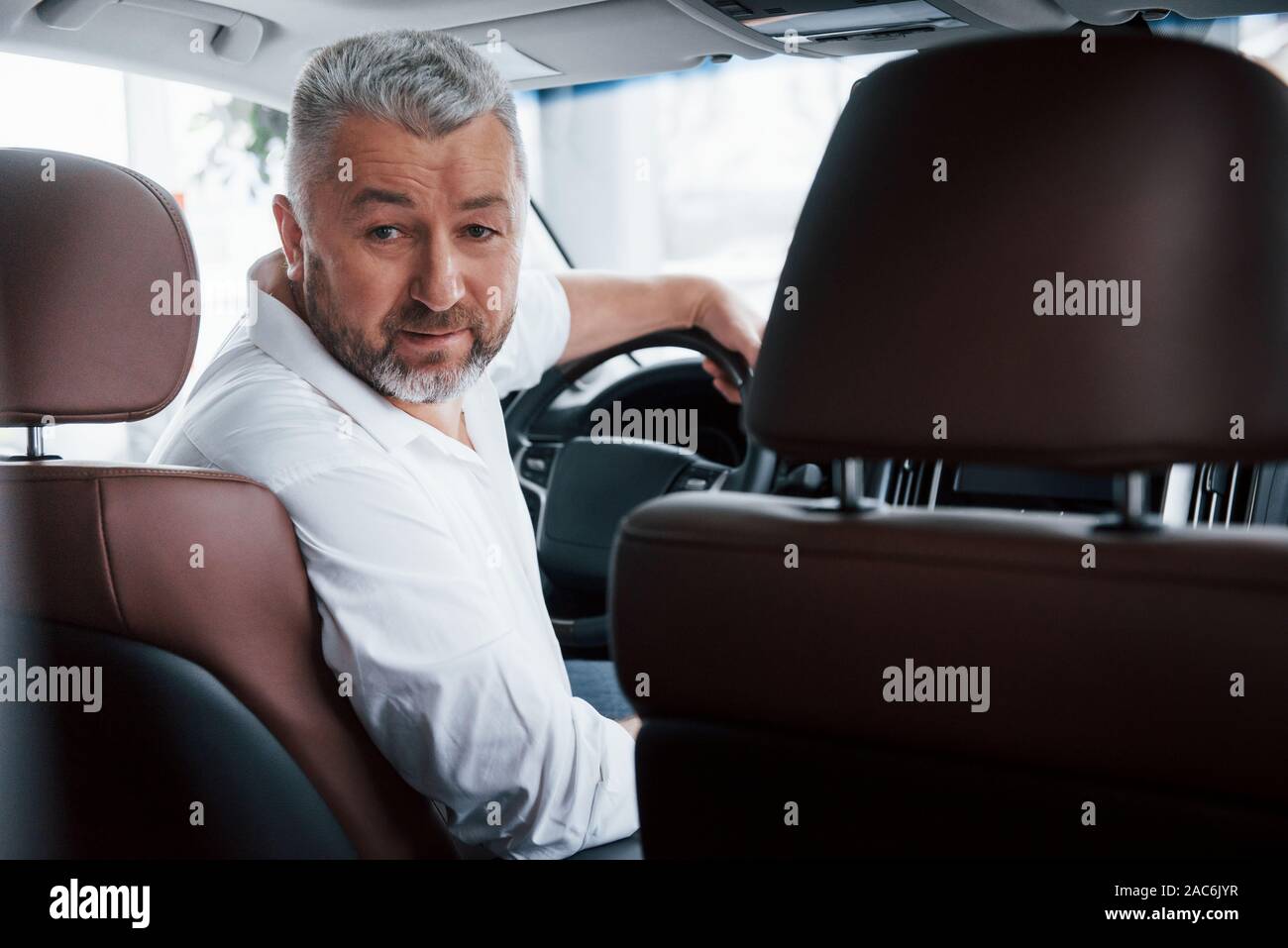 Freudige bärtiger Mann im weißen Hemd schaut in die Kamera, während in der modernen Auto sitzen Stockfoto