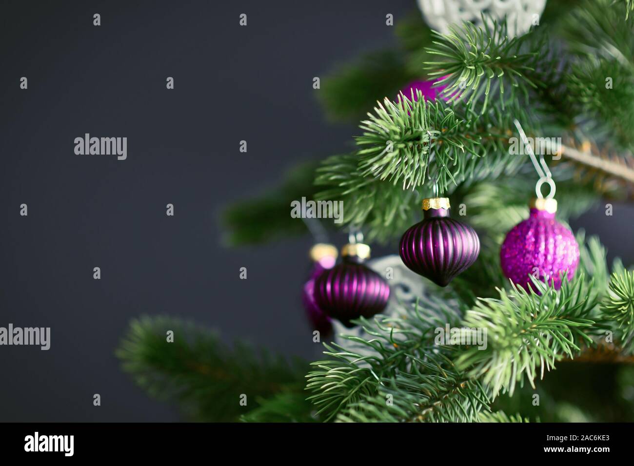 In der Nähe von schönen lila Glas baum Christbaumkugel mit geschmückten Weihnachtsbaum mit anderen saisonalen Baumschmuck auf dunklen schwarzen Hintergrund Stockfoto