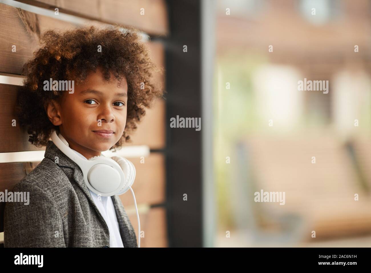 Portrait von afrikanischen Jungen mit lockigem Haar und mit Kopfhörern bei Kamera schaut beim Stehen im Freien Stockfoto