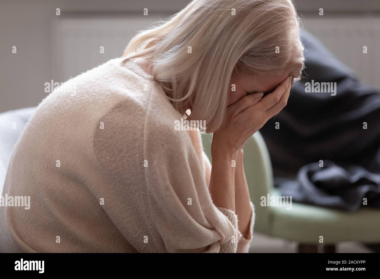 Ältere Frau versteckt Gesicht mit den Händen auf der Couch sitzt weinend Stockfoto