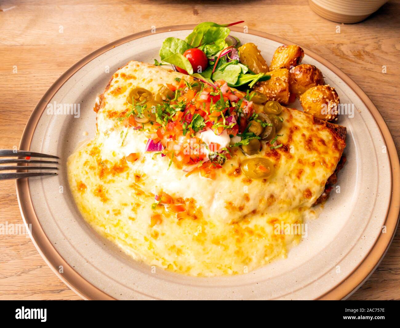 Vegetarische Enchilada Puy-linsen in Tortilla mit geschmolzenem Käse saure Sahne salsa und Jalapeños mit Salat und Sesam Kartoffeln Stockfoto