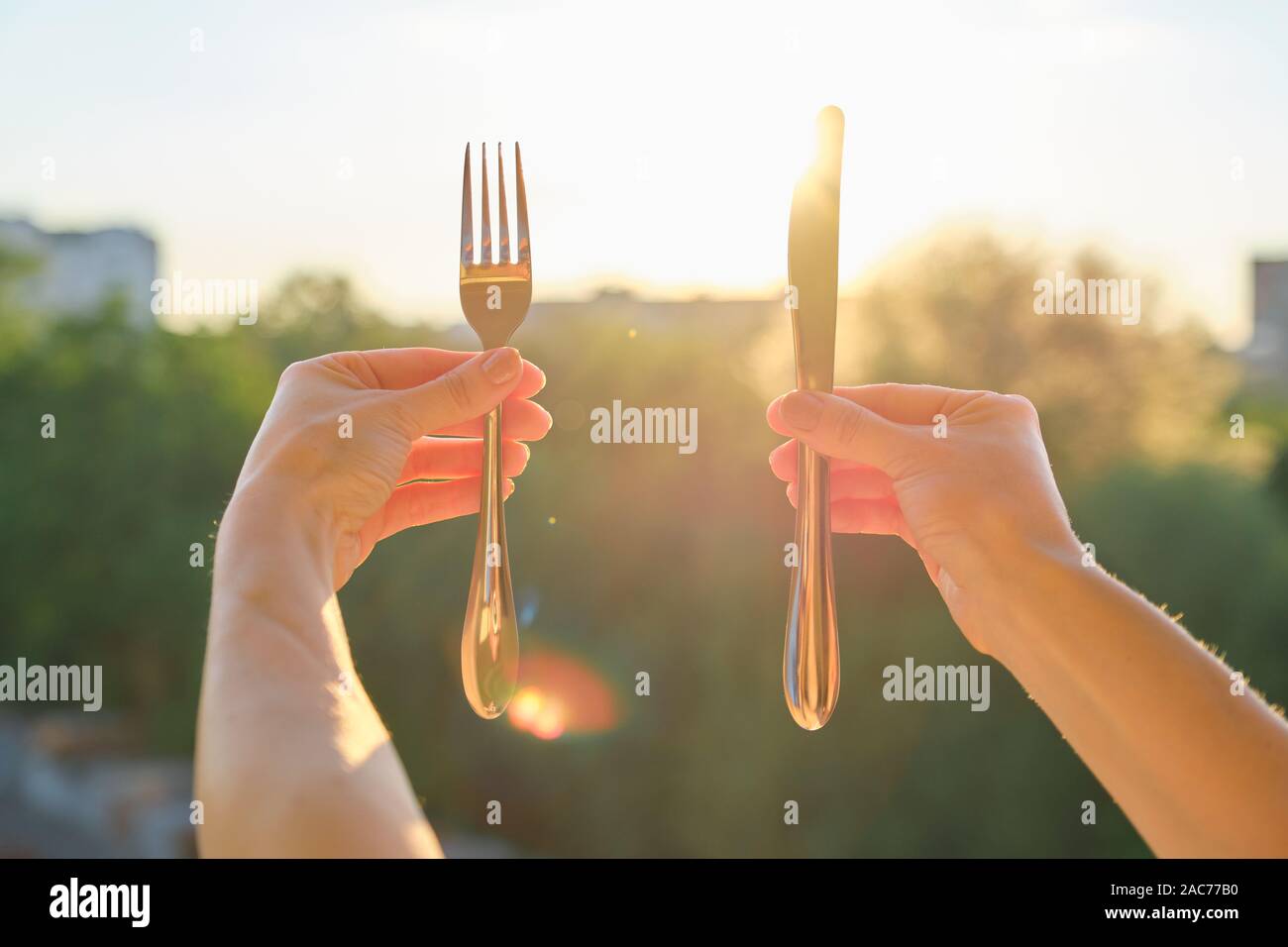 Stahl Metall Glänzendes Messer und Gabel in einem womans Hand, Hintergrund, Sonnenuntergang, abend stadt Stockfoto
