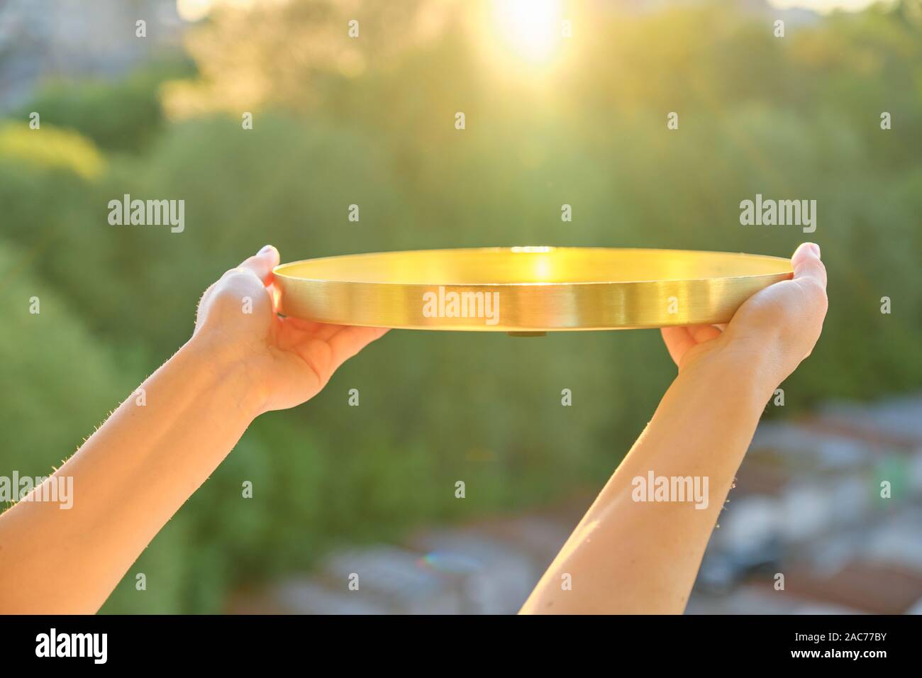 Runde goldenen Messing Metall Fach in der womans Hände, Hintergrund, Sonnenuntergang, abend stadt Stockfoto
