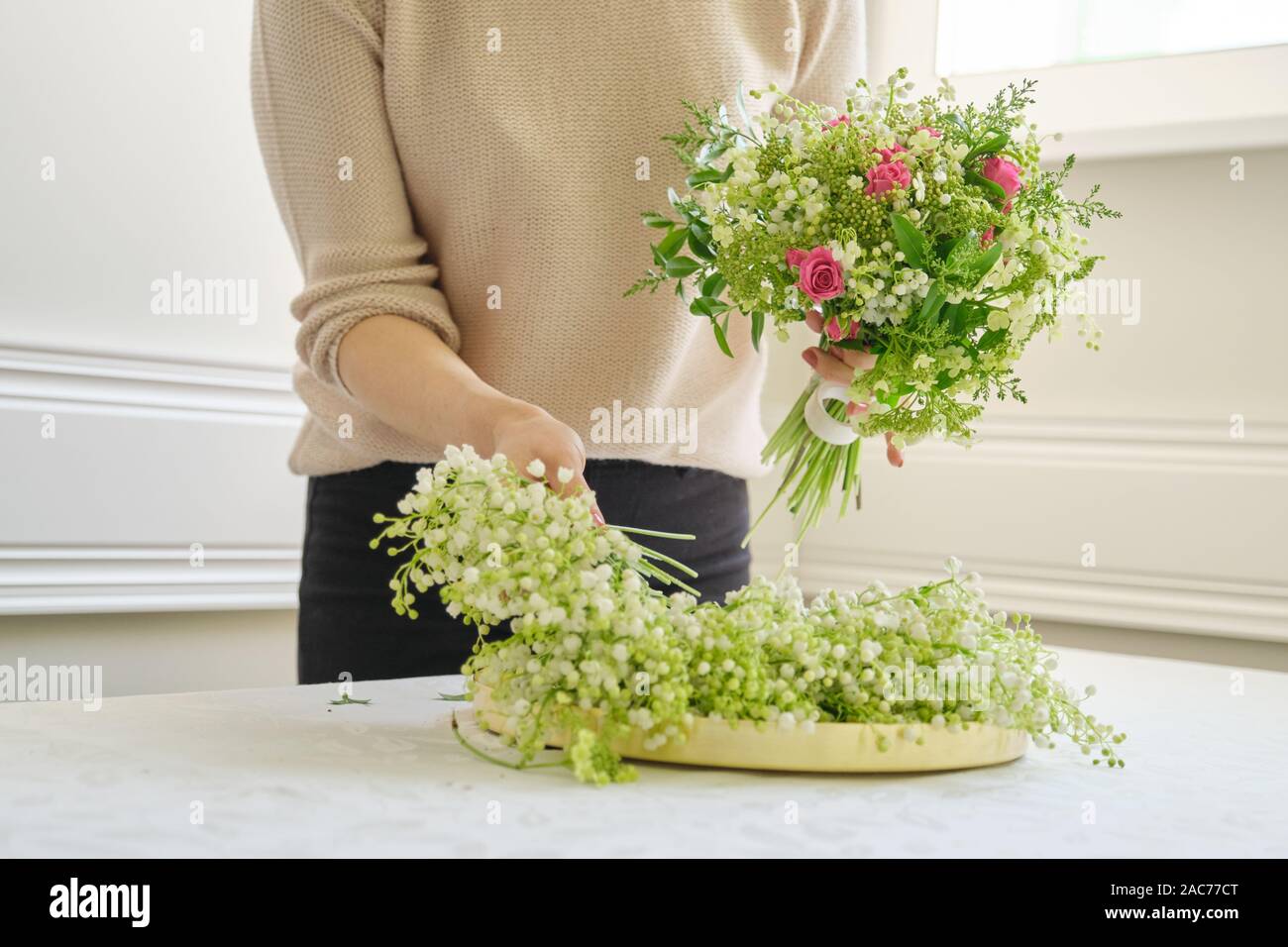 Frau florist mit unterschiedlichen Blumen auf dem Tisch, Bouquet, Blumen von Maiglöckchen, Rosen, viburnum. Floristik, Florist, f Stockfoto