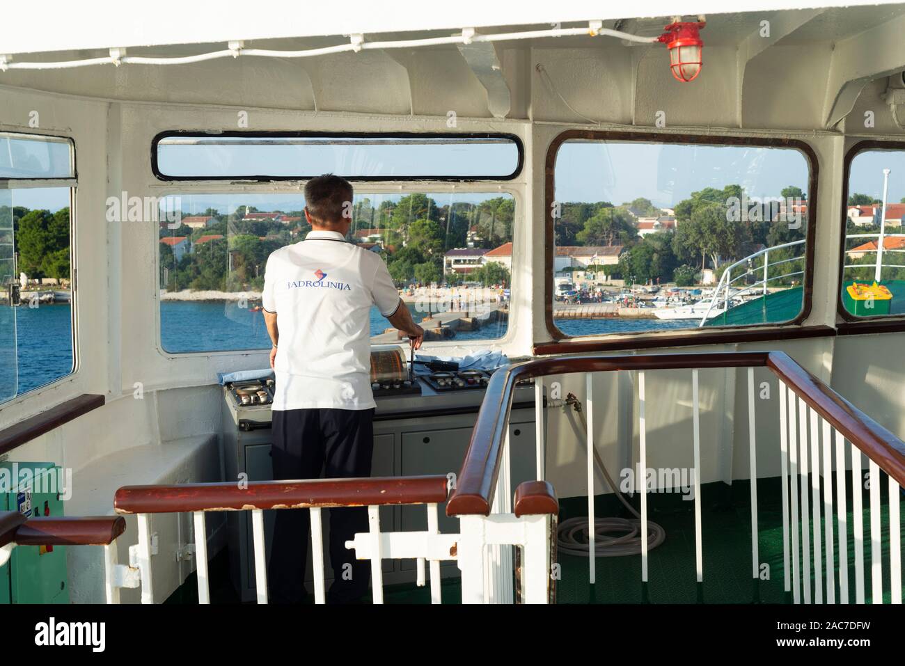 Der Steuermann einer Autofähre steht auf der Brücke und leitet das Schiff an der Pier im Hafen auf der Insel Silba, Kvarner Bucht, Kroatien Stockfoto