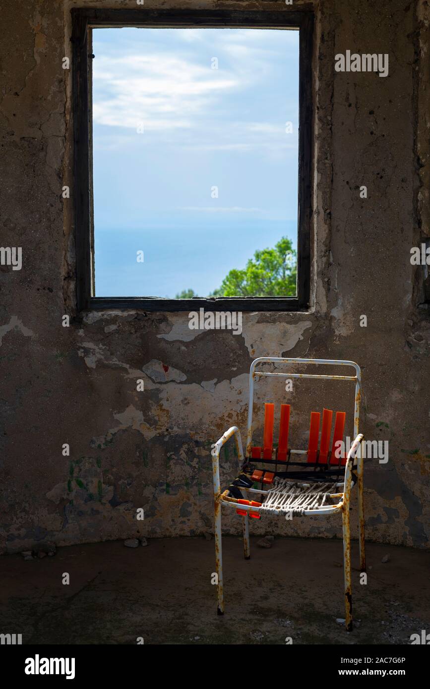 Kaputter Stuhl vor dem Fenster auf, das von den Ruinen einer Festung aus dem 19. Jahrhundert an der Hum Berg in der Nähe der Stadt Velu Luka, Insel Korcula, Kroatien Stockfoto