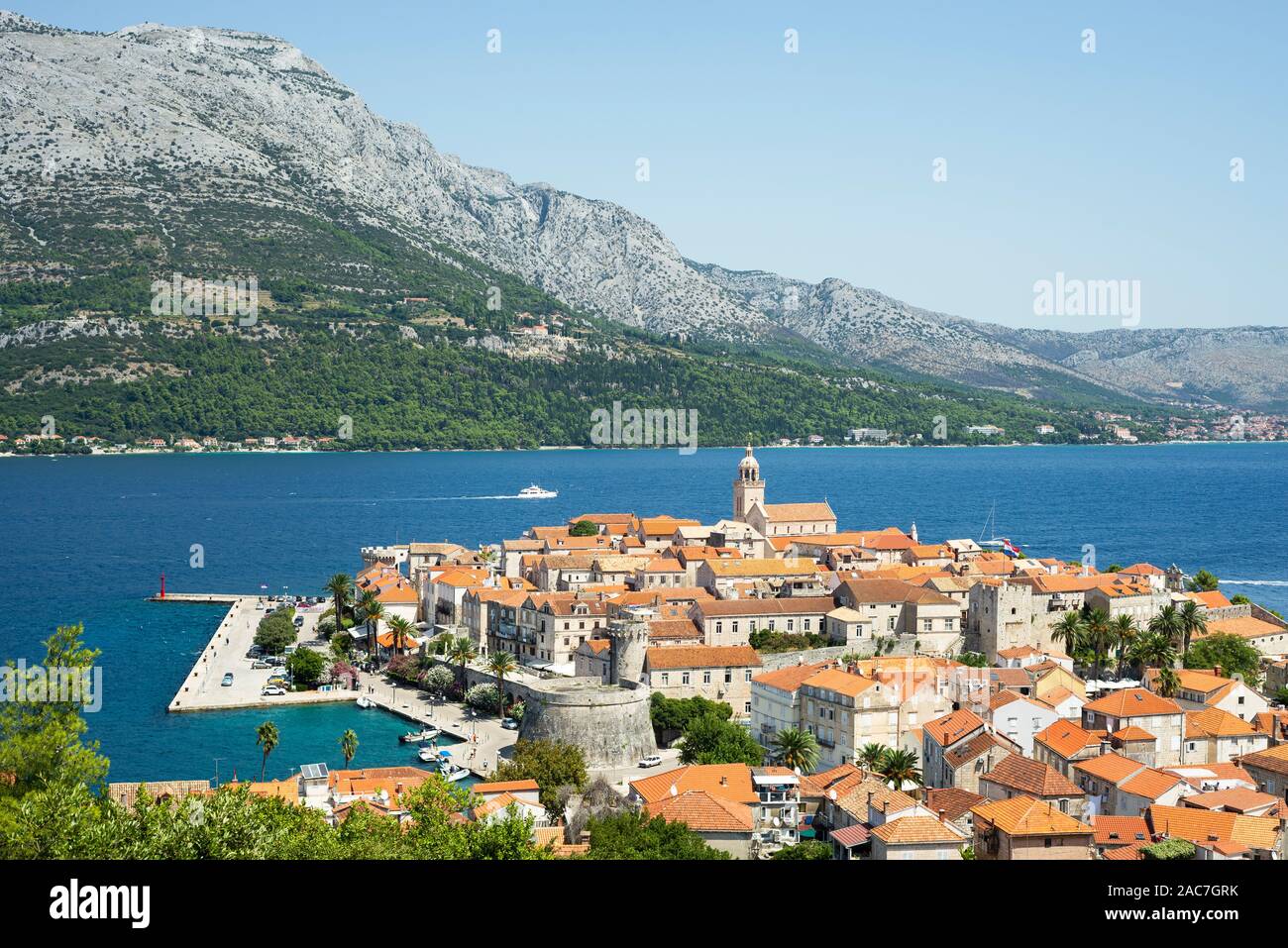 Die mittelalterliche Altstadt von Korcula vor der bergigen Halbinsel Pelješac im Sonnenschein, Süddalmatien, Kroatien Stockfoto