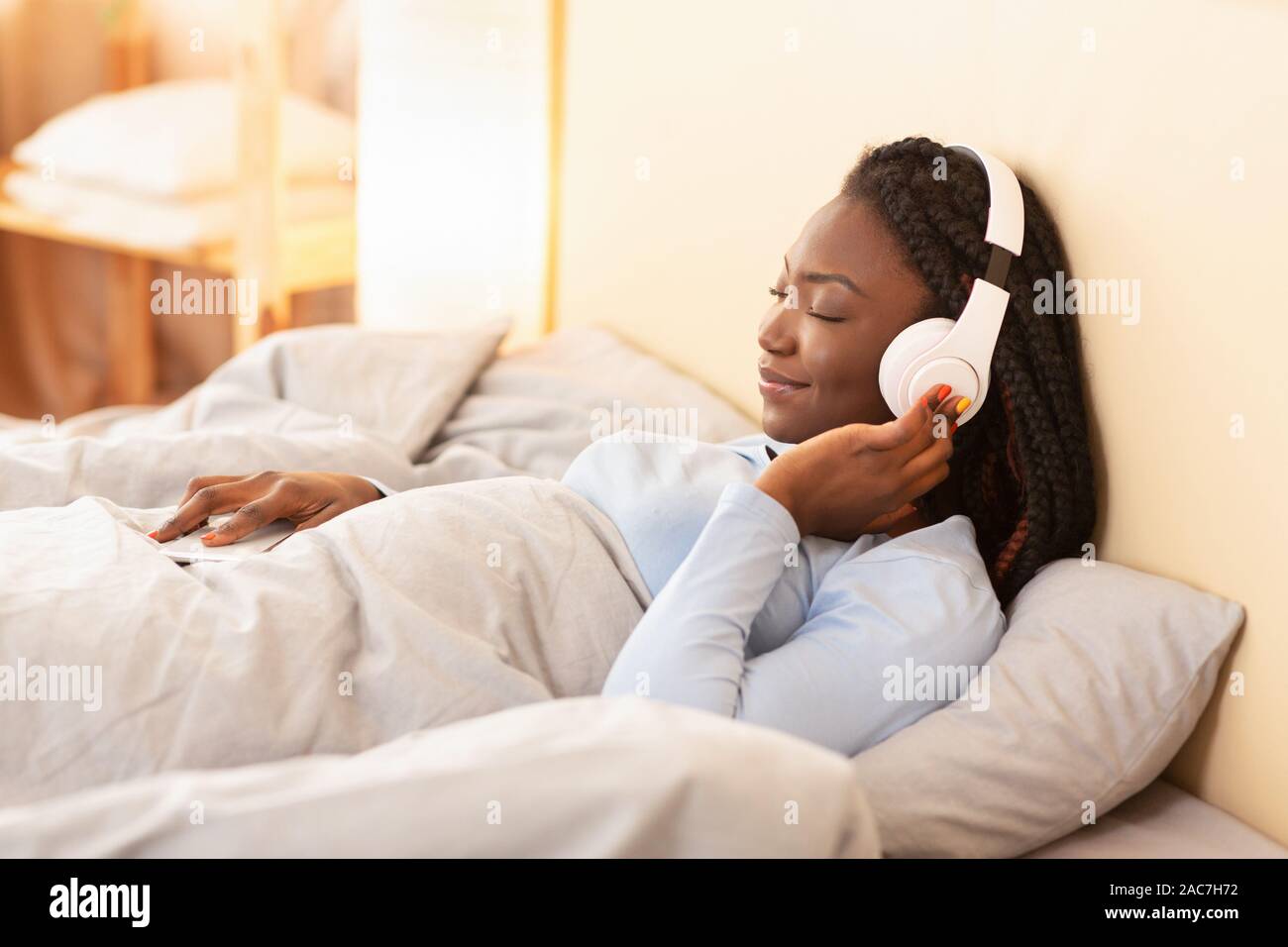 Dame in Kopfhörer anhören Hörbuch im Bett liegend Indoor Stockfoto