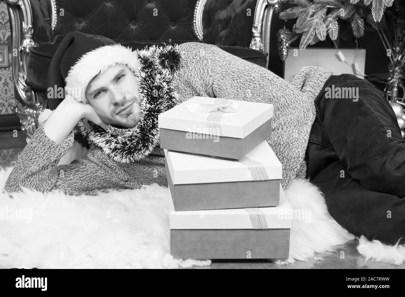 Macho in santa hut mit vorhandenen Feldern auf dem flauschigen Teppich entspannen. Mann bereit Party zu feiern. Neues Jahr, Weihnachten, Eve. Winterurlaub Feier. Boxing Day Konzept Stockfoto