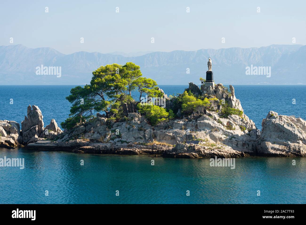 Eine weiße Madonna Statue steht auf einem Felsen im Hafen von orebic vor dem Hintergrund der Berge der Makarska Riviera, Peljesac, Kroatien Stockfoto