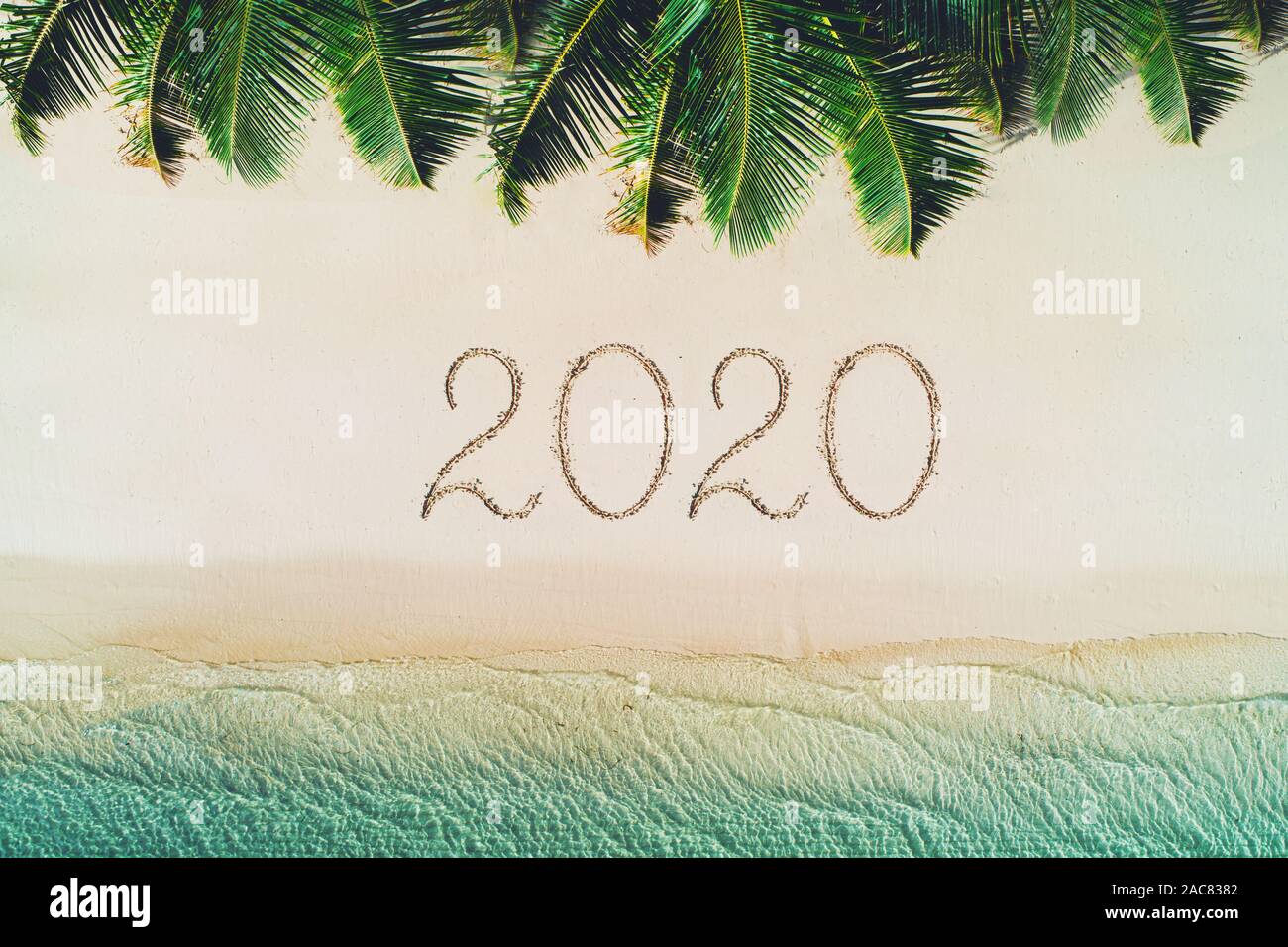 Frohes neues Jahr Strand Konzept, 2020 in den Sand geschrieben. Sommerurlaub auf der tropischen Insel. Palmen und Meer Wellen. Stockfoto