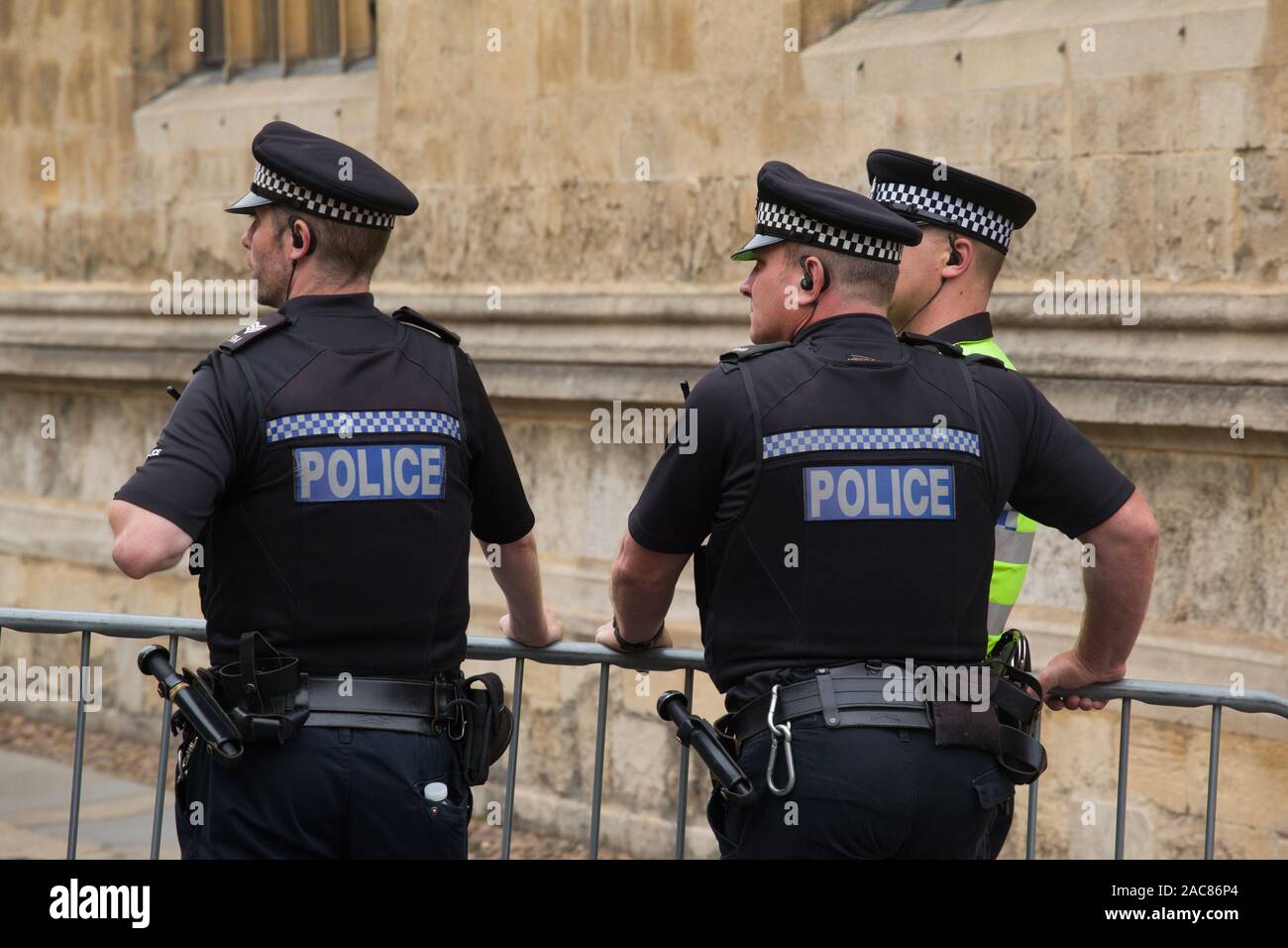 Drei uniformierte Polizisten in kurzen Ärmeln tragen Kappen mit Headsets und tragen utility Gürtel mit Gummiknüppeln überwachen eine Demonstration Stockfoto