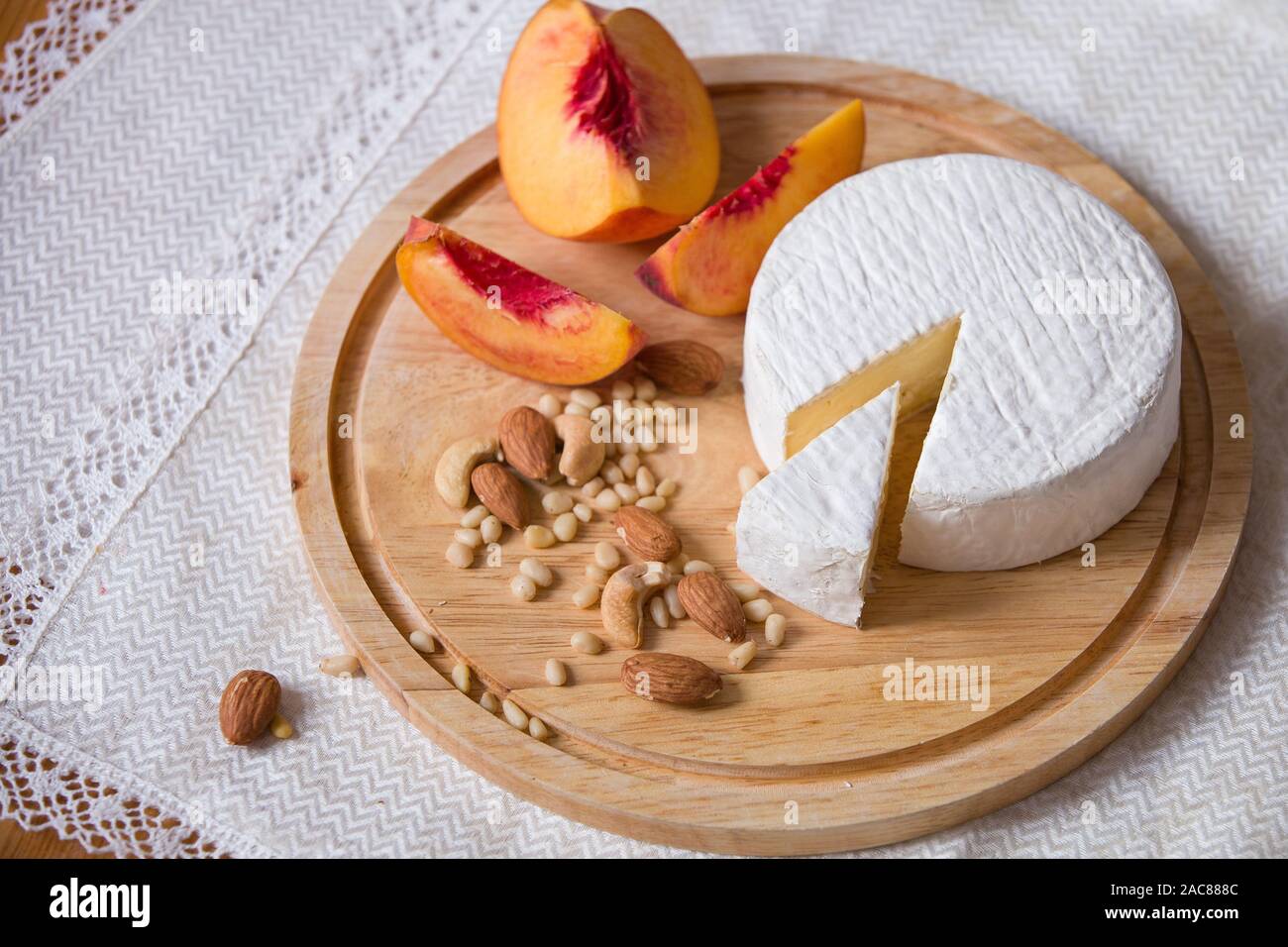 Weiß köstliche hausgemachte camambert Käse auf einem Holzteller serviert mit Mandeln, Cashew, Pinienkernen und Pfirsich. Dessert für ein Abendessen mit der Familie. Stockfoto