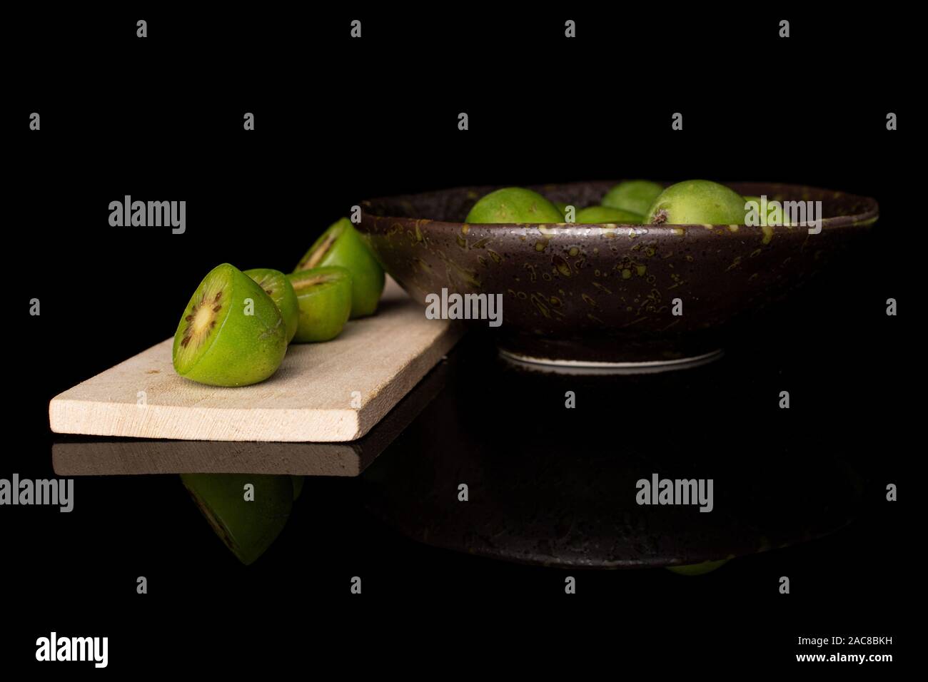 Gruppe der Menge ganze vier Hälften von Hardy Grüne Kiwi auf Holz Schneidebrett in glasierte Schüssel auf schwarzem Glas isoliert Stockfoto