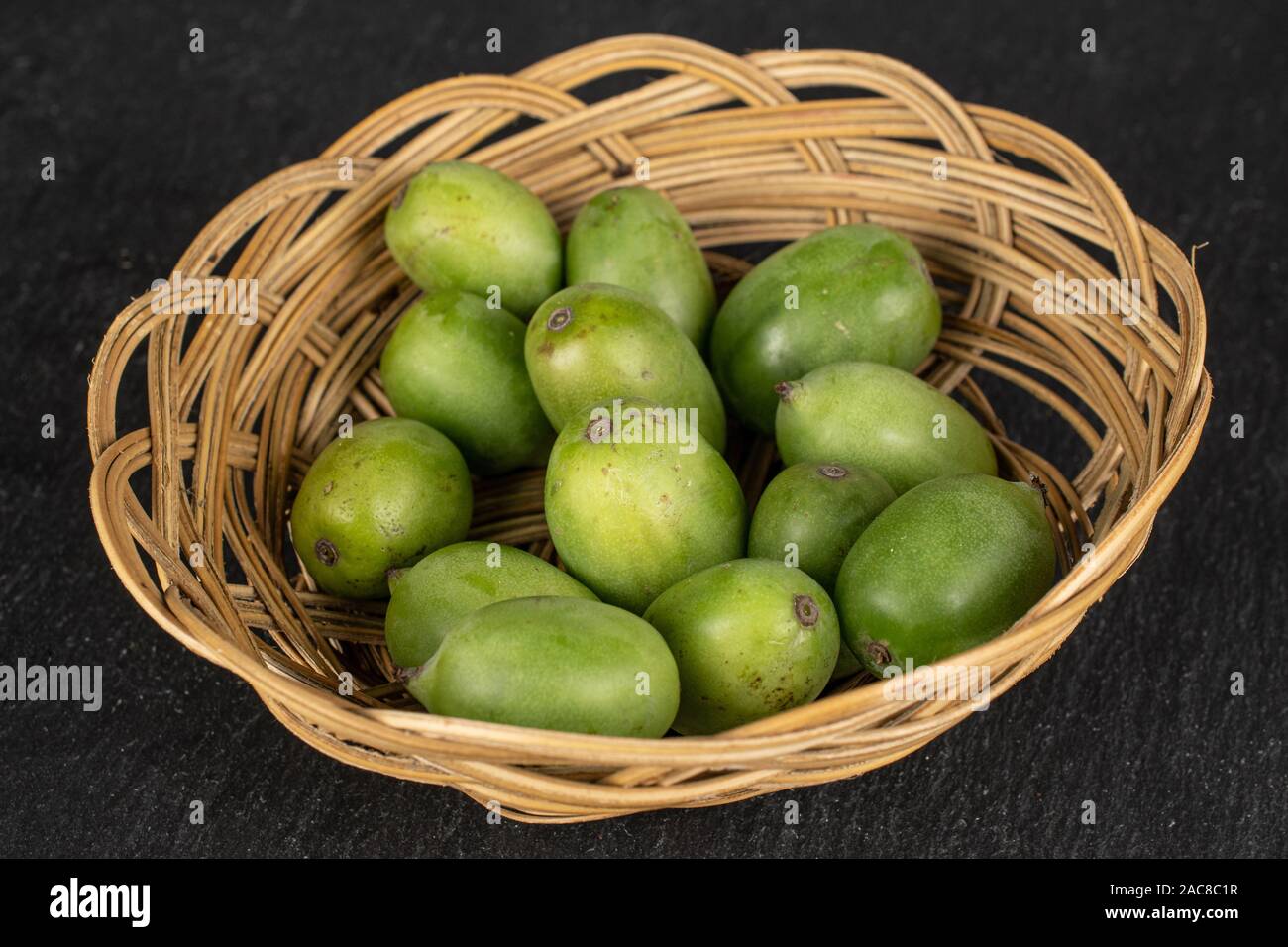 Menge ganze Hardy Grüne Kiwi in Runde Rattan Schüssel auf grauem Stein Stockfoto