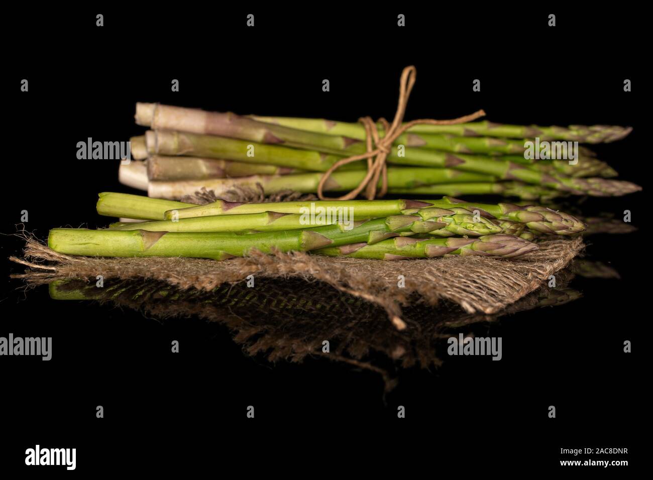 Menge ganze Frische, gesunde grüner Spargel mit Stroh Seil und Jutegewebe auf schwarzem Glas isoliert Stockfoto
