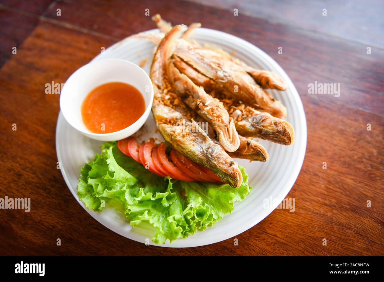 Gebratener Fisch mit Gemüse Salat Tomaten und Soße auf weiße Platte Holztisch - süßwasserfische Mekong Andere Namen Sheatfishes Siluriformes Silur Stockfoto