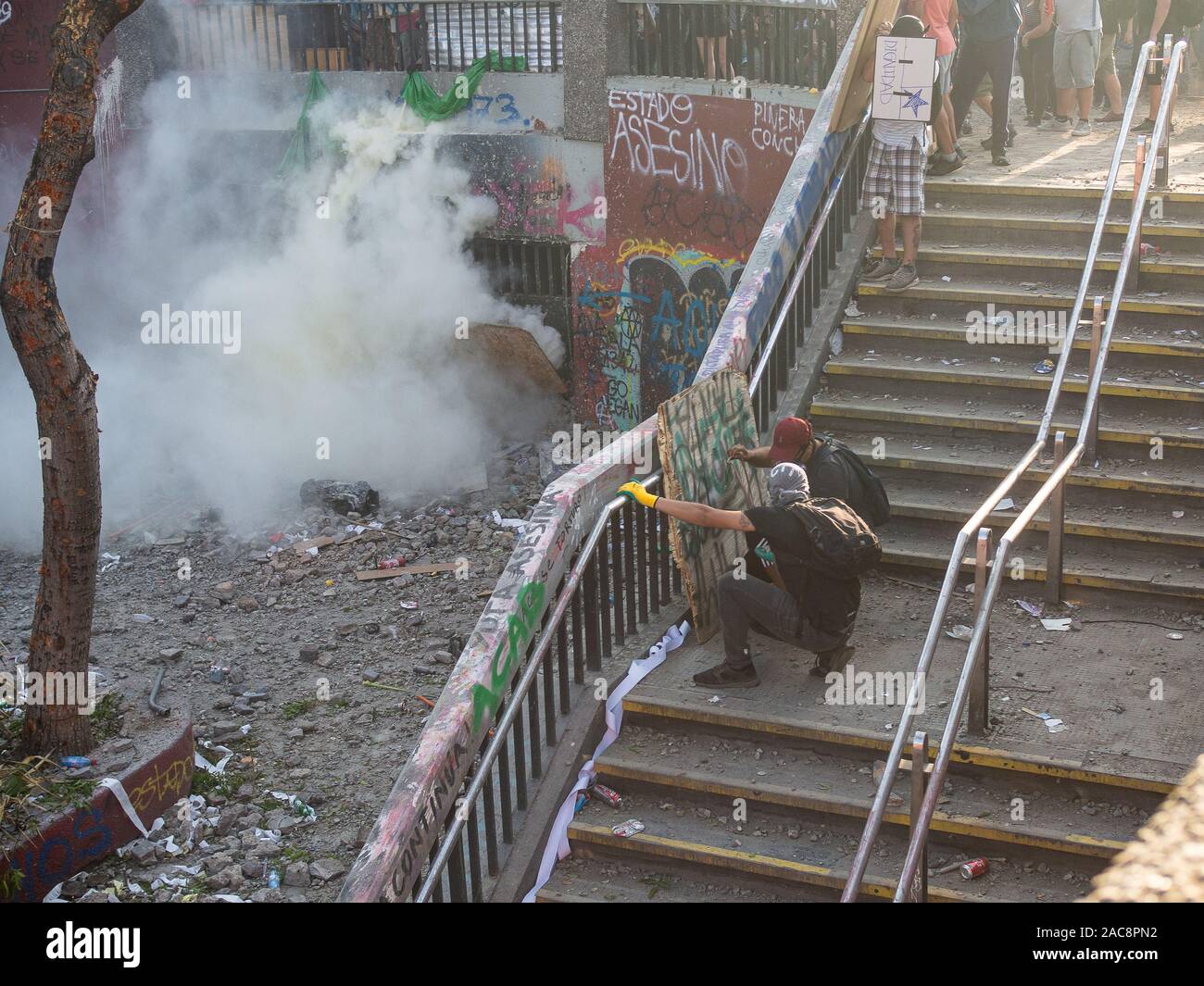 Santiago de Chile NOV 12 / Erste Zeile Demonstranten gegen die Polizei, die hinter der Metall Türen verborgen sind, trowing gas Bomben reißen Stockfoto