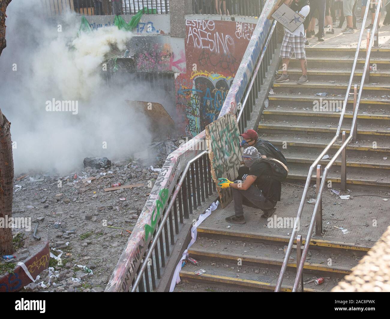 Santiago de Chile NOV 12 / Erste Zeile Demonstranten gegen die Polizei, die hinter der Metall Türen verborgen sind, trowing gas Bomben reißen Stockfoto