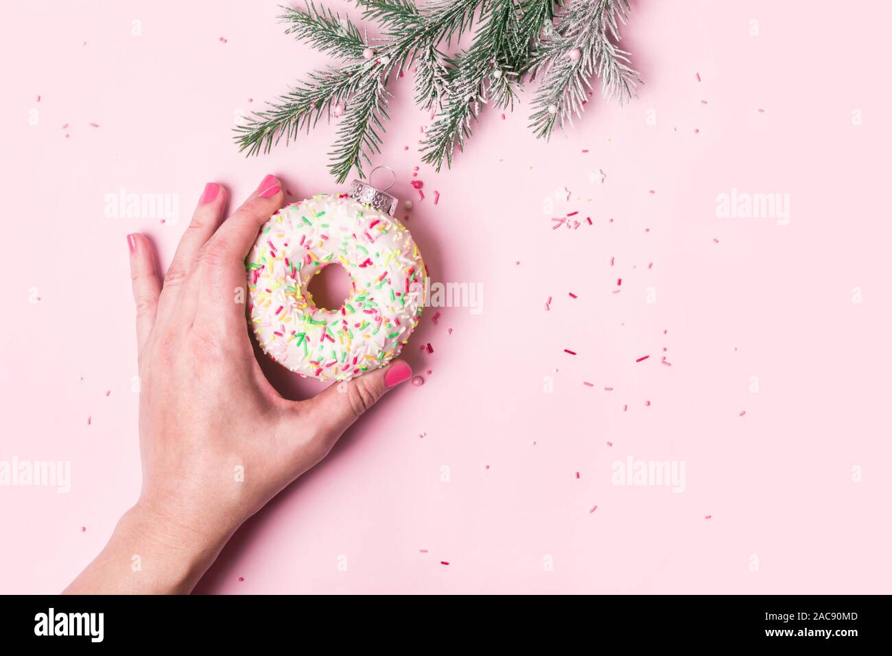Weibliche Hand hängt Christmas Ball von donut auf rosa Hintergrund gemacht. Weihnachten kreative Konzept. Stockfoto