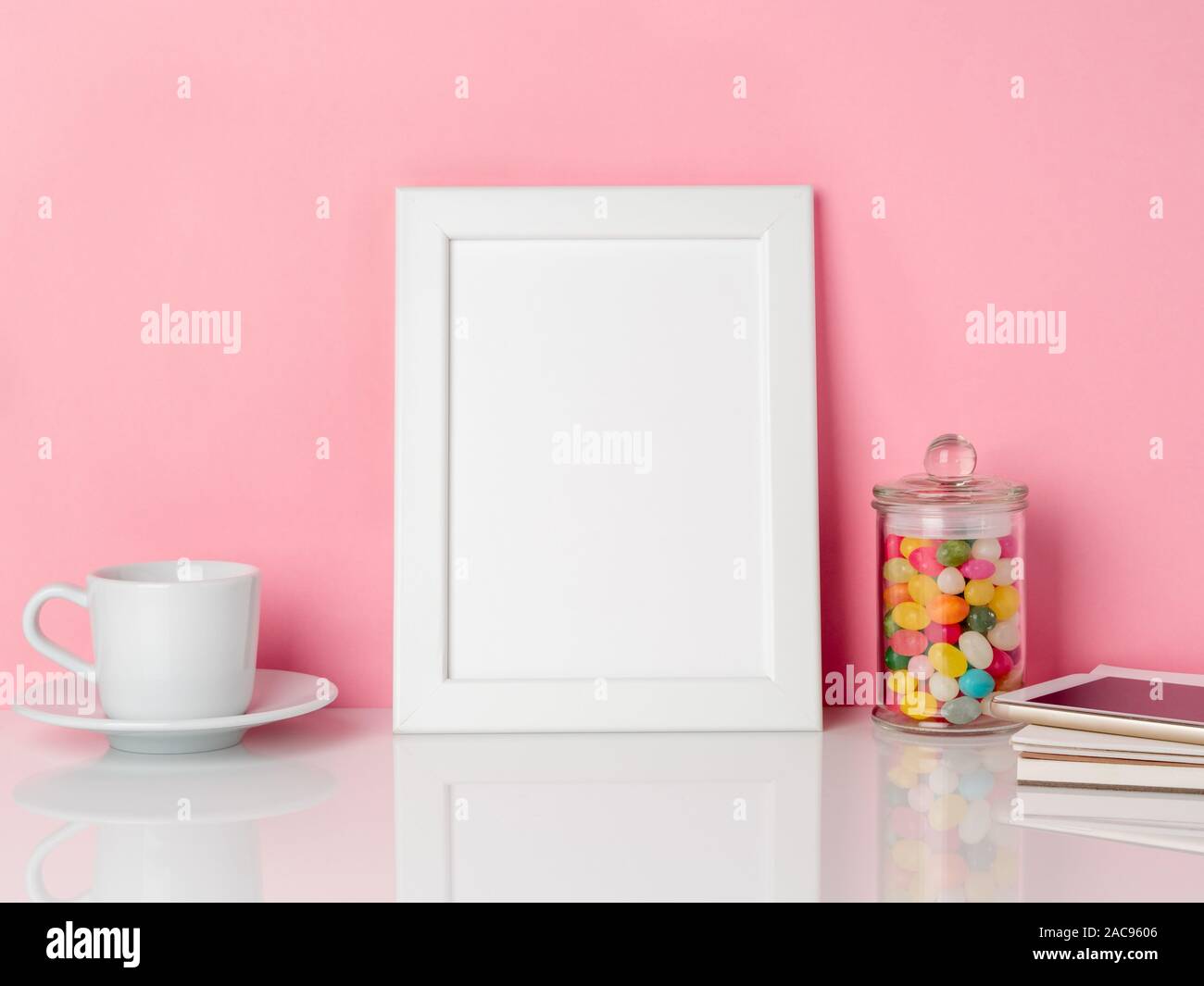 Leeren weißen Rahmen und Candys im Glas, Tasse Kaffee oder Tee auf einem weißen Tisch gegen die rosa Wand mit Kopie Raum Stockfoto