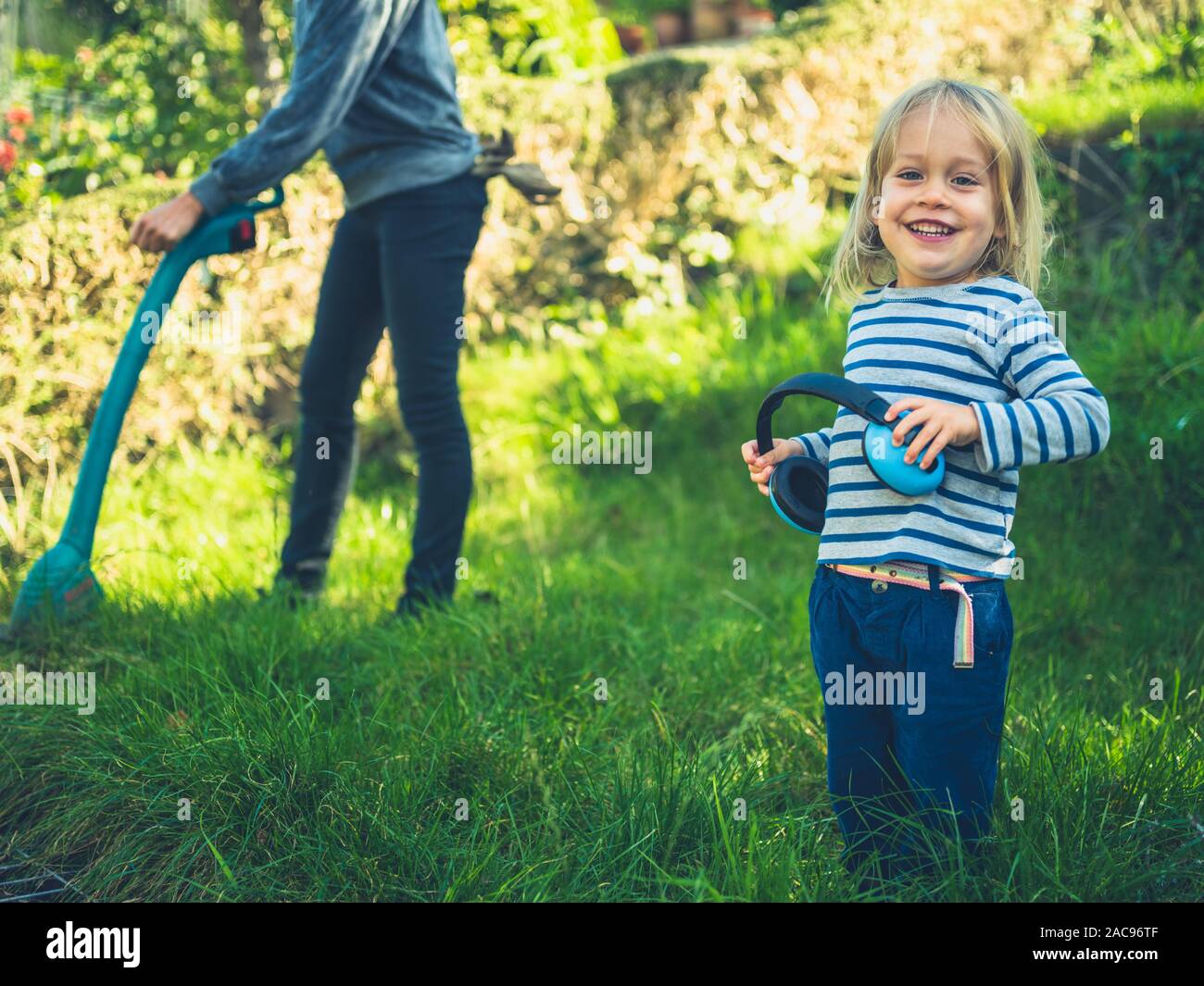 Ein kleines Kind schaut seine Mutter ein Gras strimmer in Ihrem Garten verwenden Stockfoto