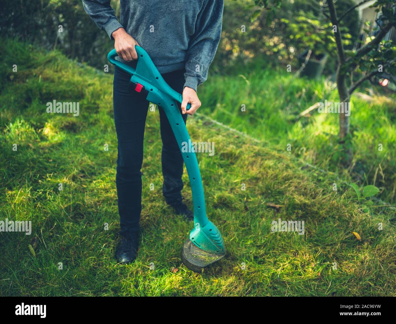 Eine junge Frau ist schneiden den Rasen mit einem Gras strimmer Stockfoto