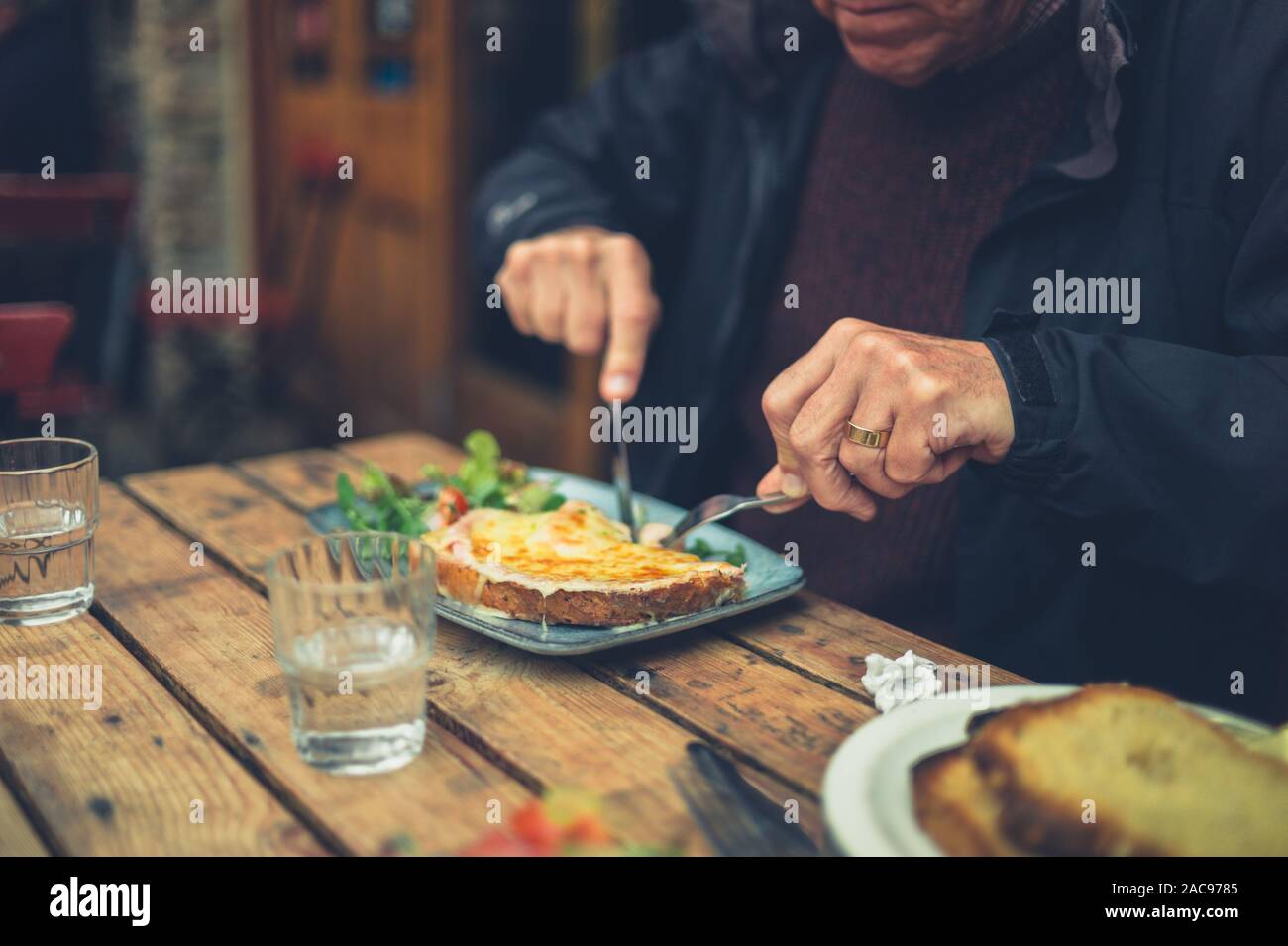 Ein älterer Mann ist Essen Käse auf Toast in einem Cafe Stockfoto