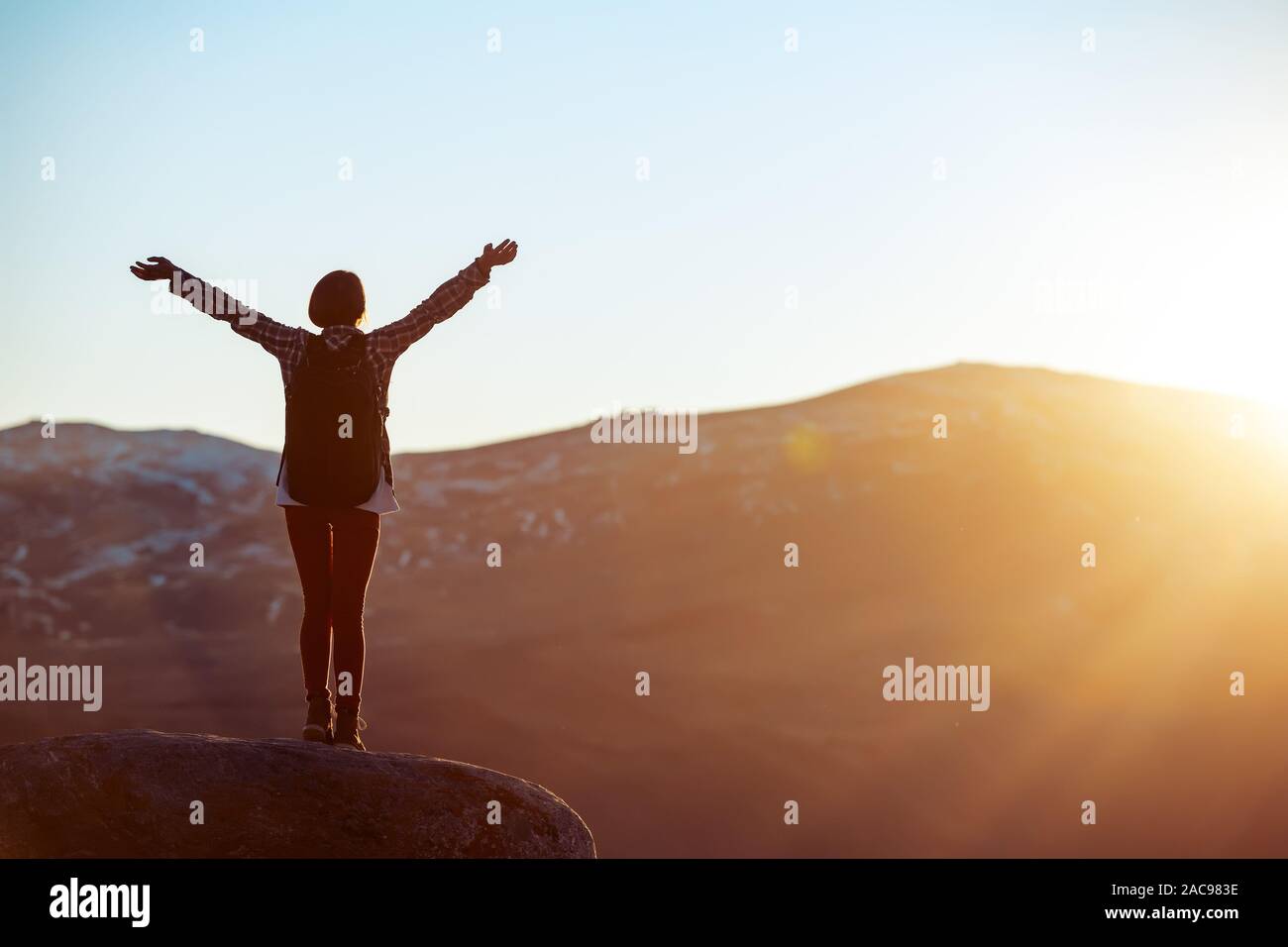 Glückliches Mädchen steht mit erhobenen Armen gegen Sonnenuntergang Licht Stockfoto