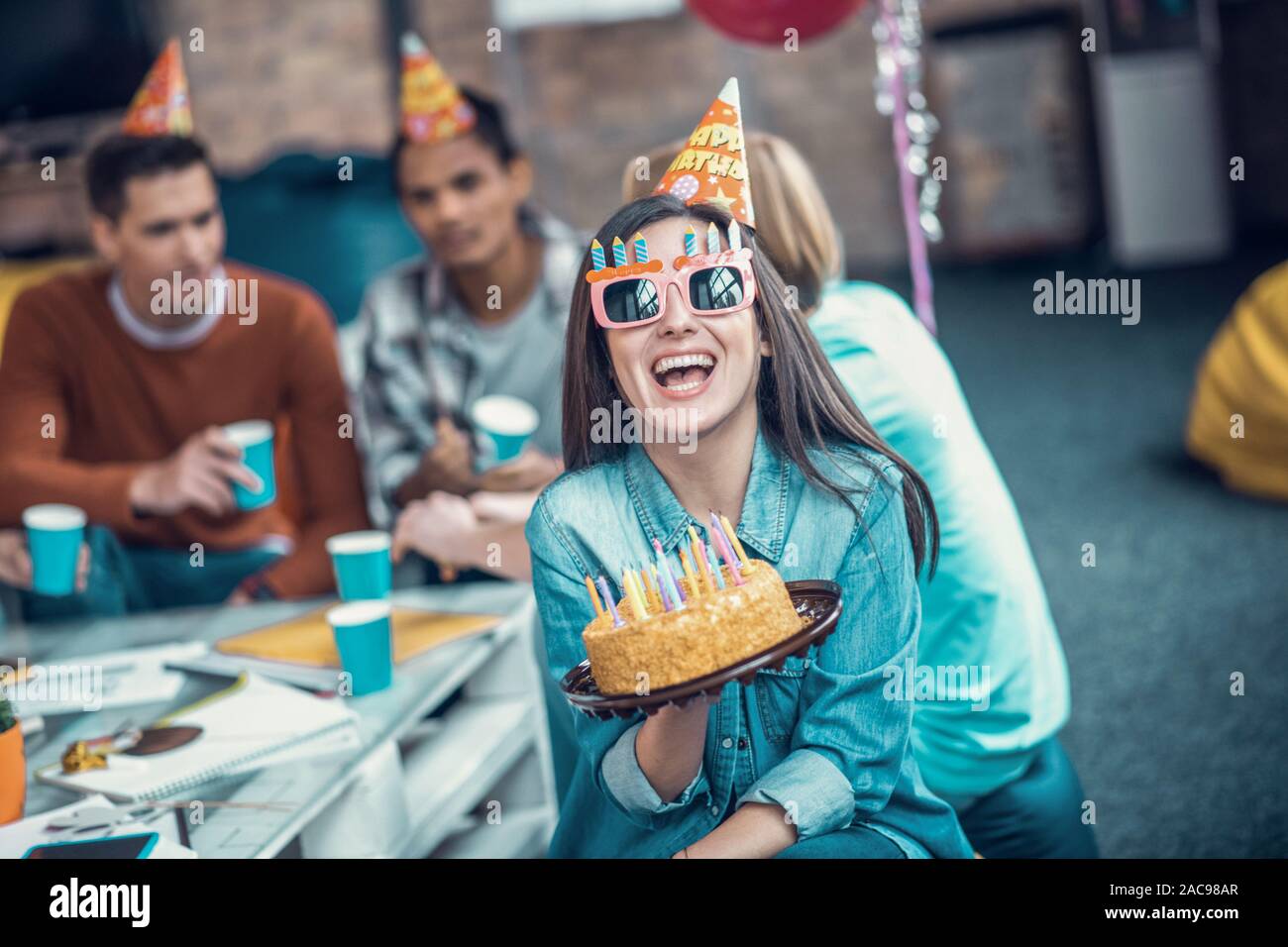 Holding Geburtstagskuchen. Schöne Mädchen Brille lächelnd, während sie Geburtstagskuchen und in Partei Stockfoto