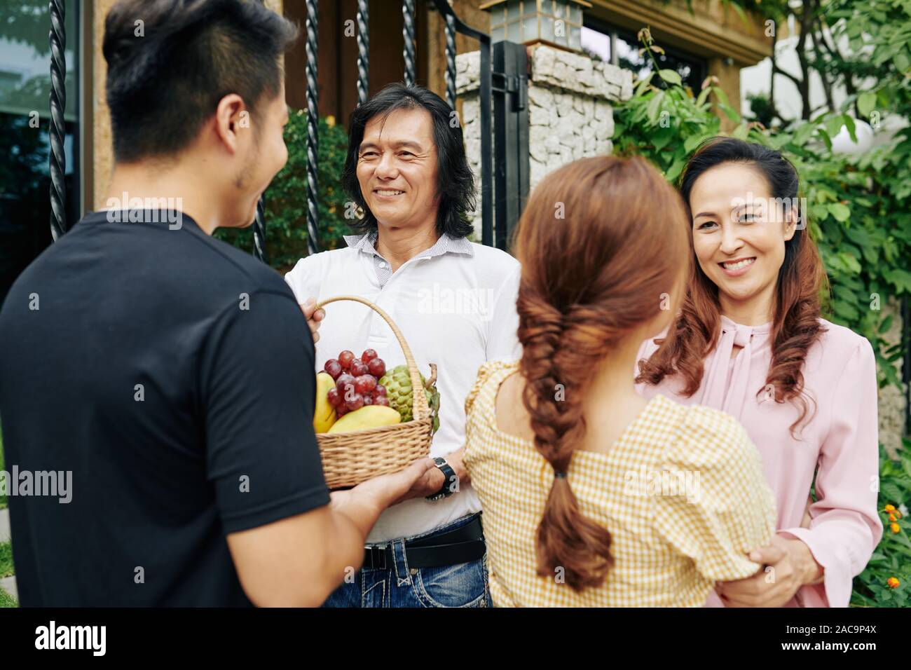 Gerne reife Vietnamesische Paare treffen ihre erwachsenen Kinder im Haus Eingang und akzeptieren Obstkorb Stockfoto