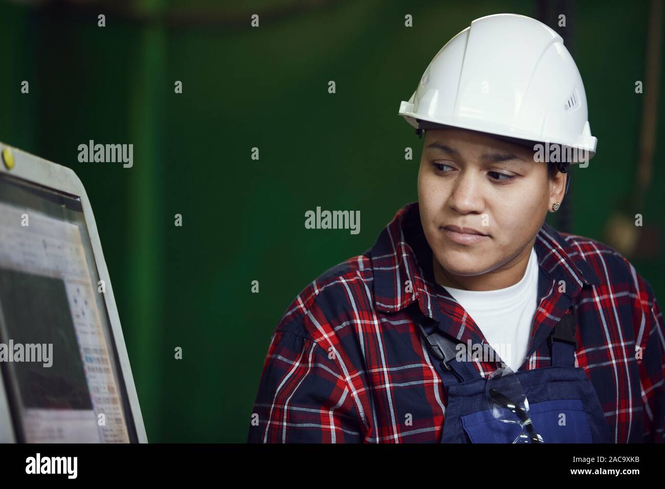 Kopf und Schultern Portrait von Mixed-race Frau tragen, hardhat auf Kontrollmonitor bei Industrieanlagen, kopieren Space zu arbeiten Stockfoto