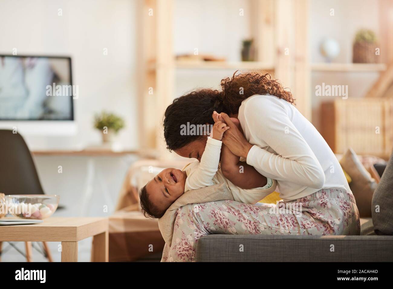 Seitenansicht Porträt der Pflege Afro-amerikanische Mutter küssen cute baby boy, während zu Hause spielt, kopieren Raum Stockfoto