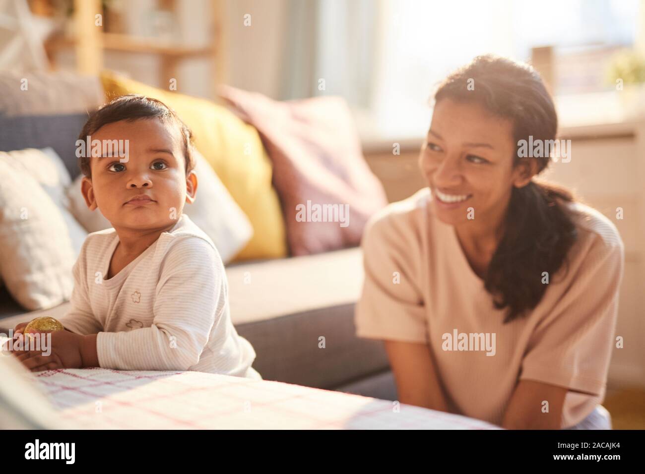Lächelnde junge Mutter sitzen und spielen mit Ihrem kleinen Kind auf dem Sofa im Zimmer Stockfoto
