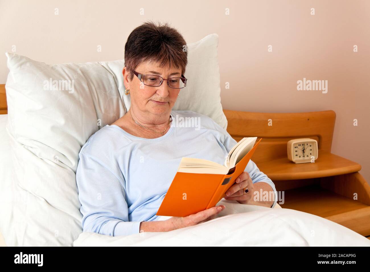 Senioren in einem Pflegeheim mit einem Buch im Bett Stockfoto