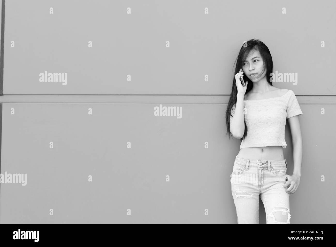 Junge schöne asiatische Jugendmädchen Gespräch am Handy beim Stehen und Denken gegen Betonmauer im Freien Stockfoto