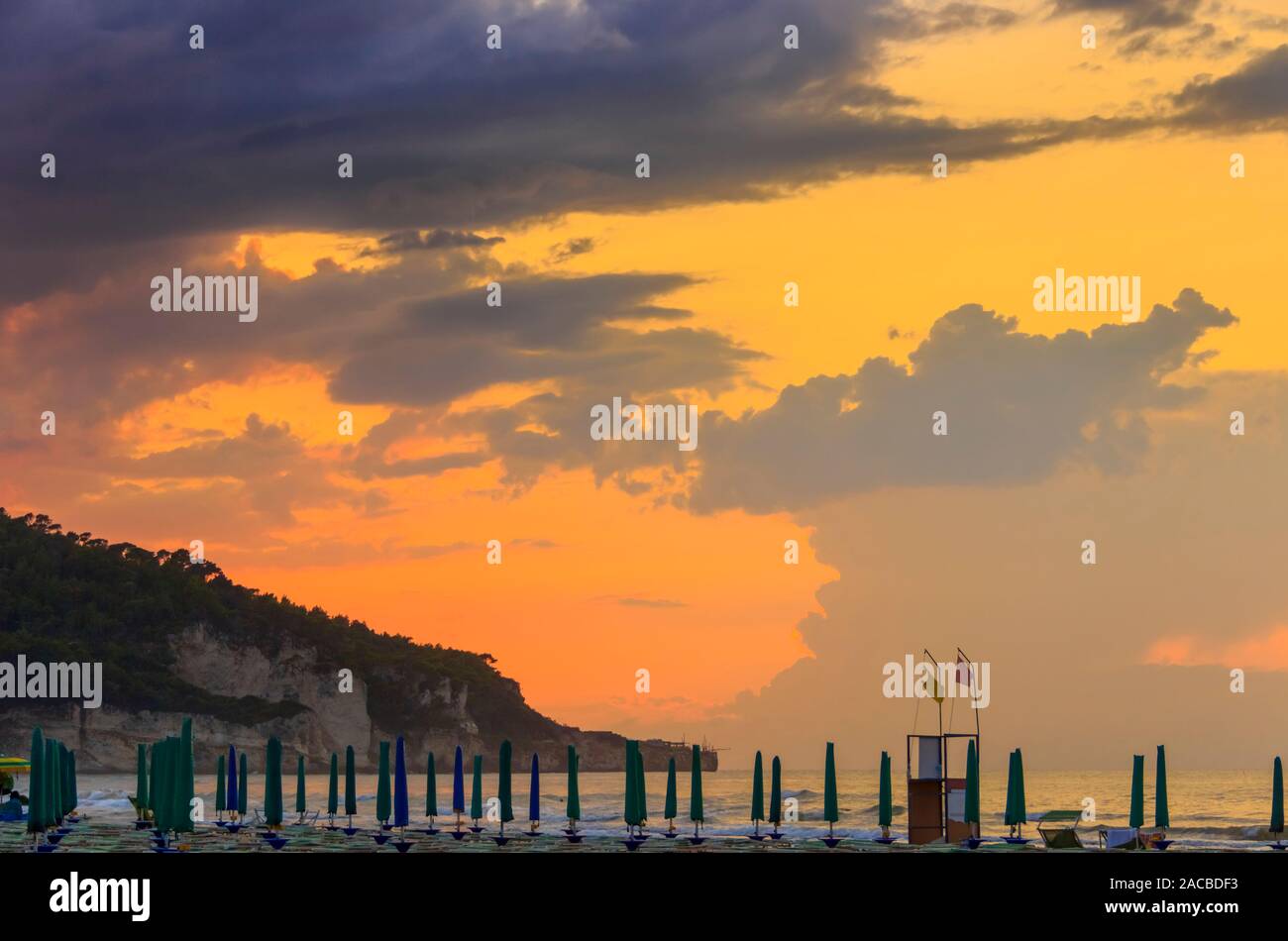 Blick auf die Bucht von Peschici bei Sonnenuntergang: Sandstrand mit Sonnenschirmen und Trebuchet, Italien (Apulien). Peschici ist berühmt für seine Badeorte. Stockfoto