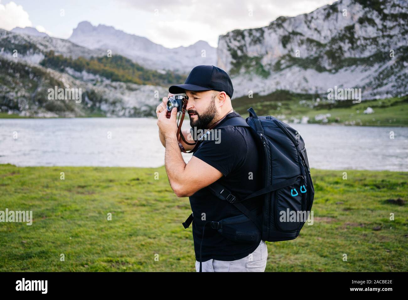 Kaukasische Mann mit Mütze und Bart macht Fotos mit einem Foto Kamera Sightseeing in einer Berglandschaft mit See Stockfoto