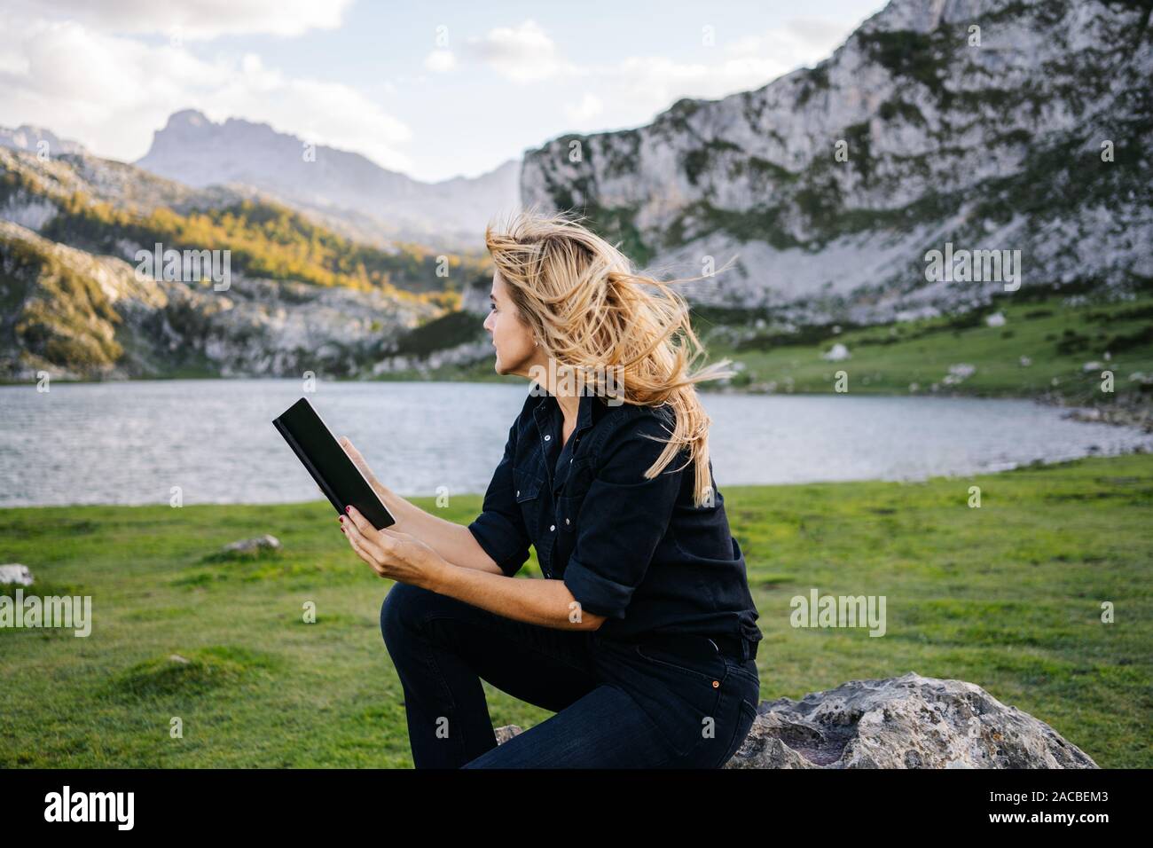 Eine schöne kaukasischen blonde Frau liest ein Buch in einer bergigen Landschaft mit See Stockfoto
