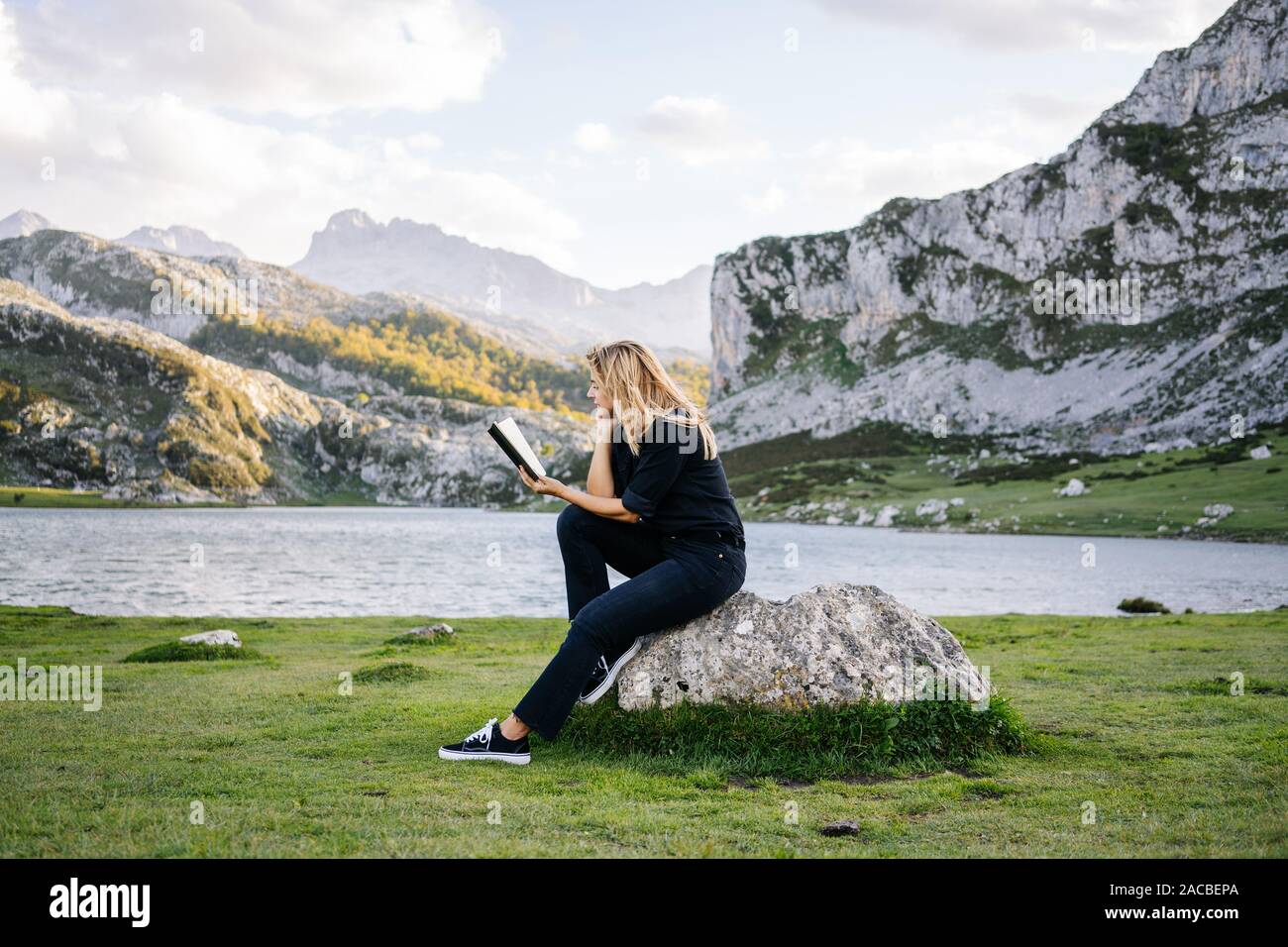 Eine schöne kaukasischen blonde Frau liest ein Buch in einer bergigen Landschaft mit See Stockfoto