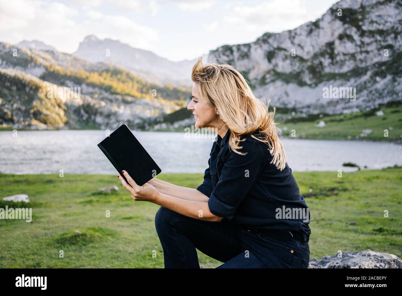 Eine schöne kaukasischen blonde Frau liest ein Buch in einer bergigen Landschaft mit See Stockfoto